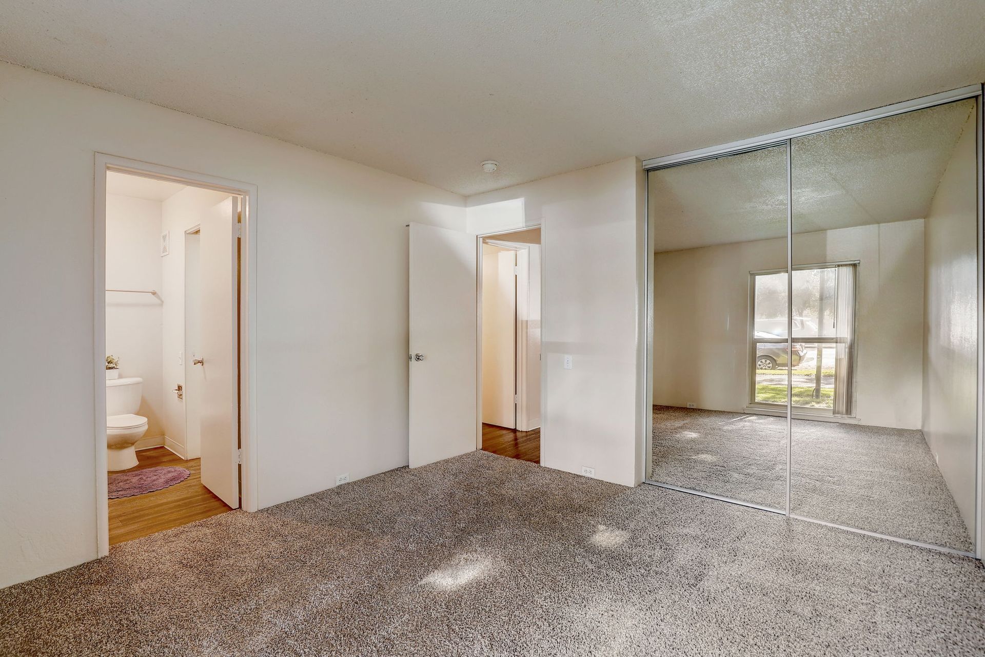 An empty bedroom with a large mirrored closet and a bathroom.