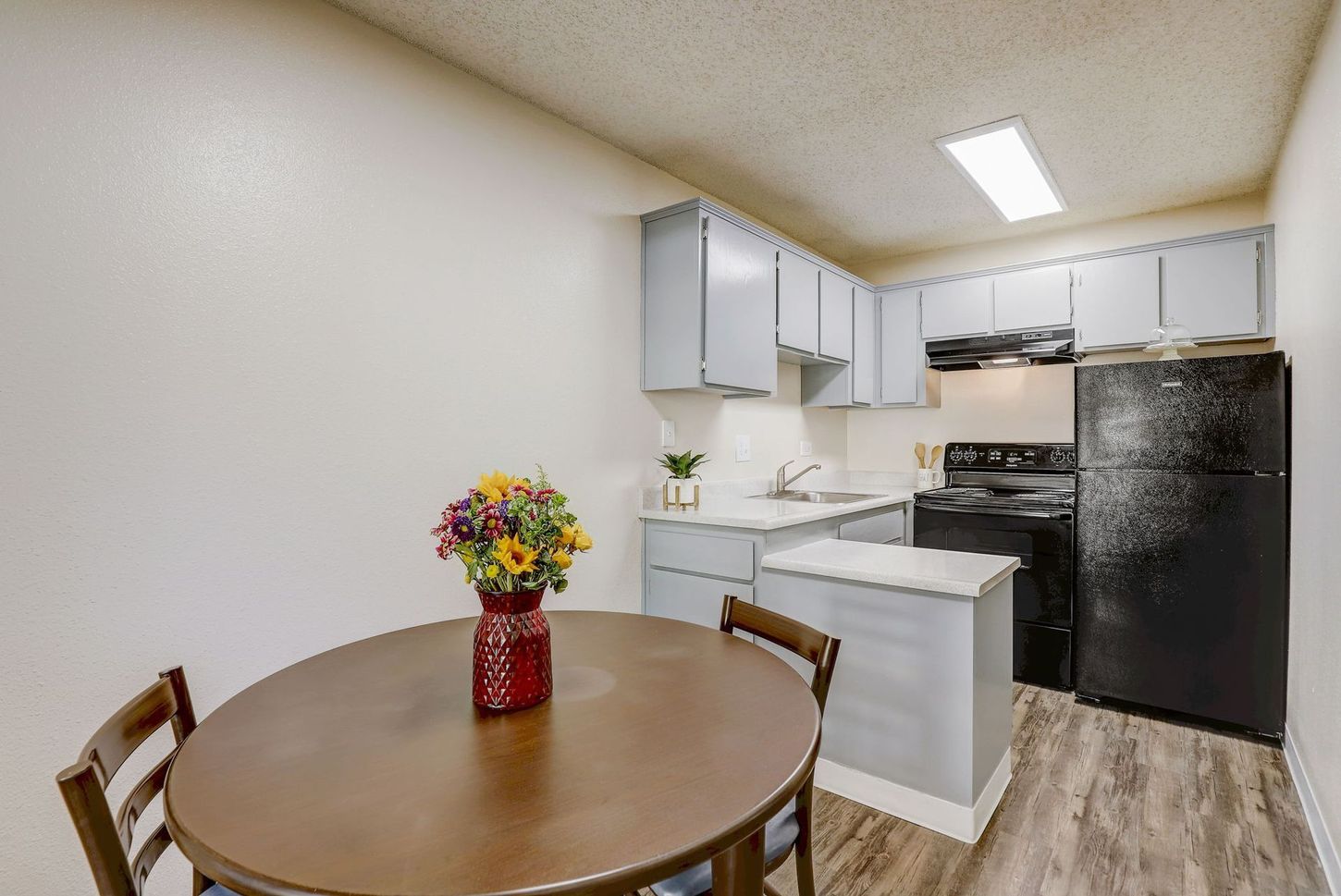 A kitchen with a table and chairs and a vase of flowers on the table.