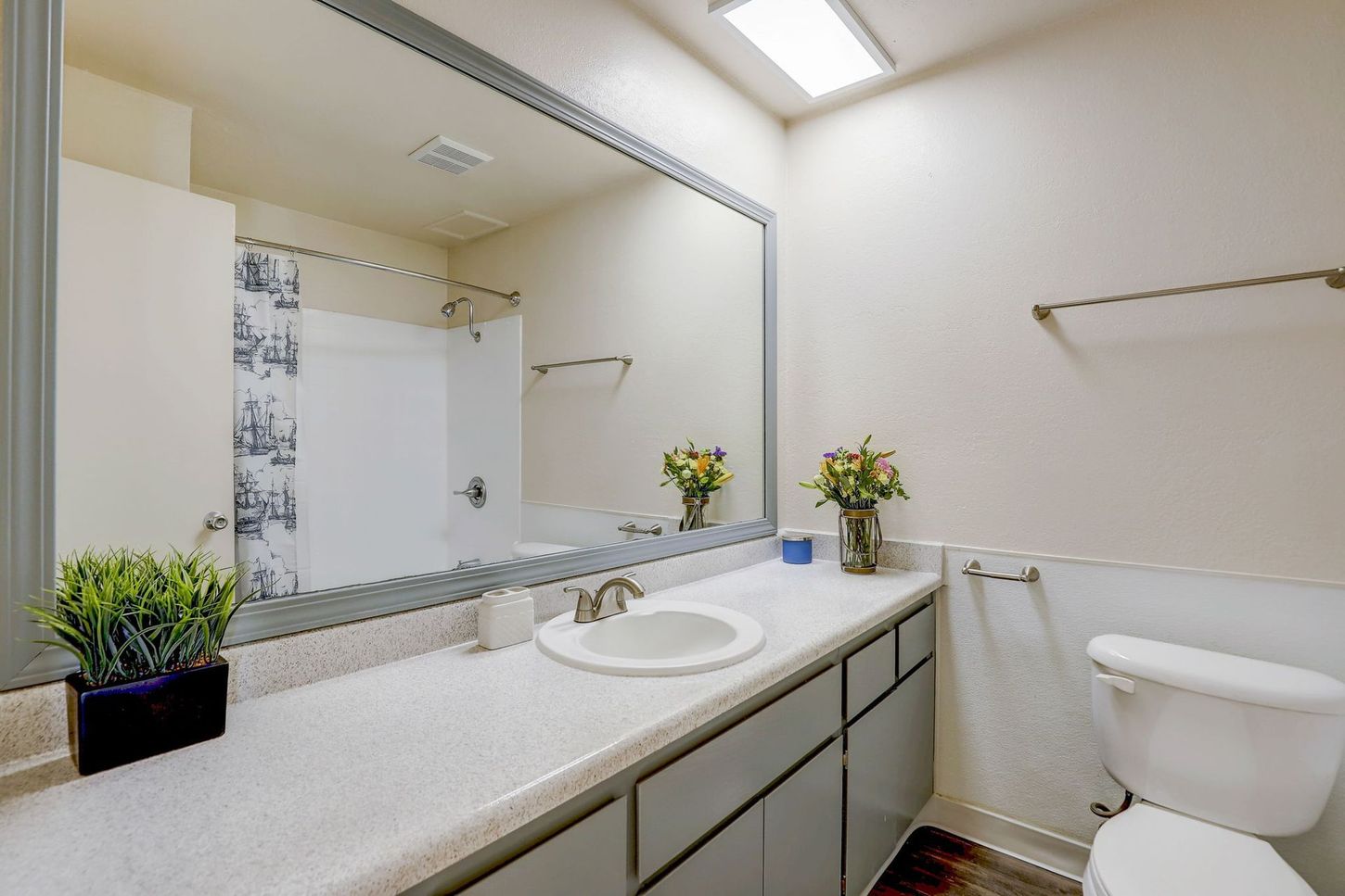 A bathroom with a large mirror , sink , toilet and shower.