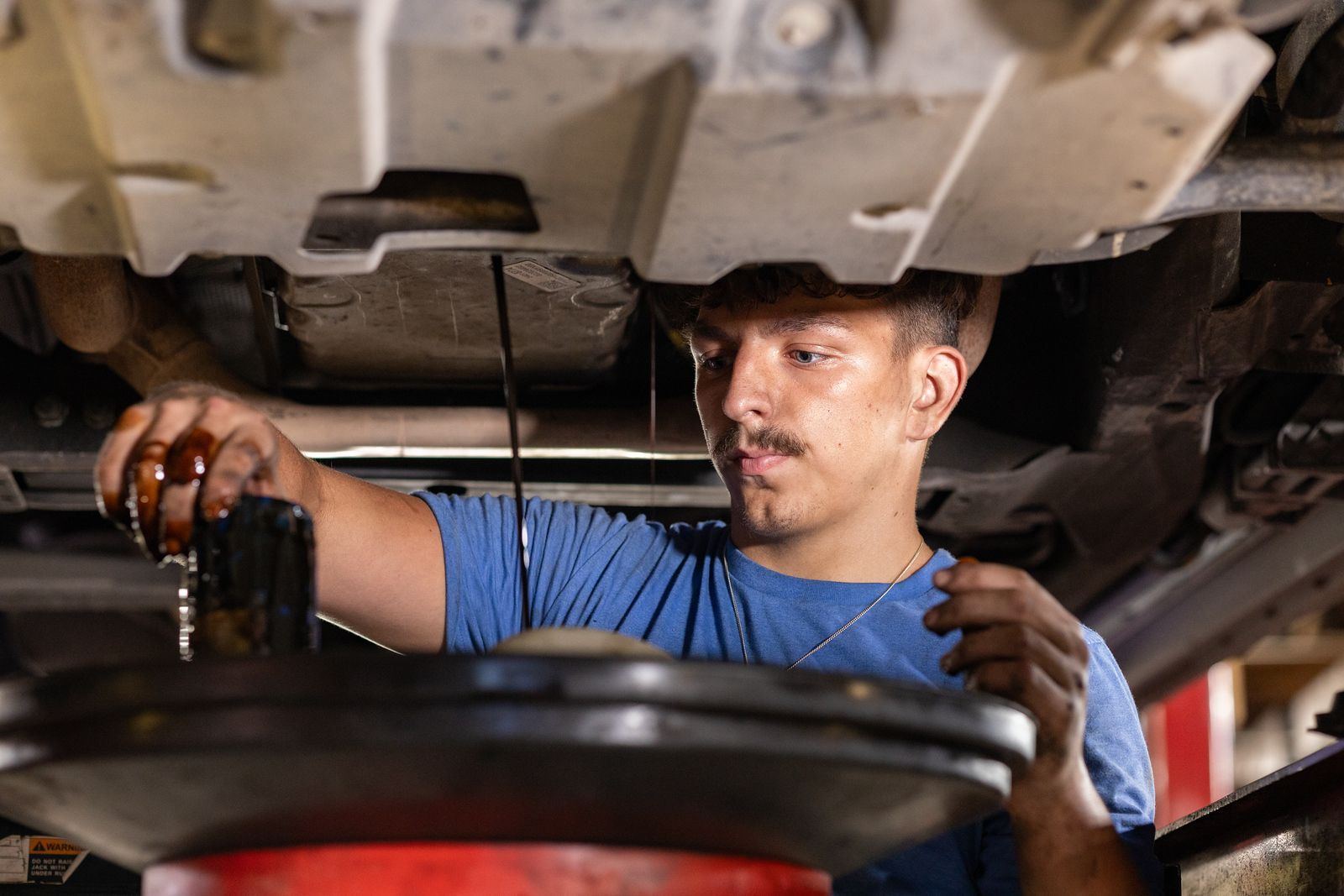 A service mechanic is working under a car in a garage.