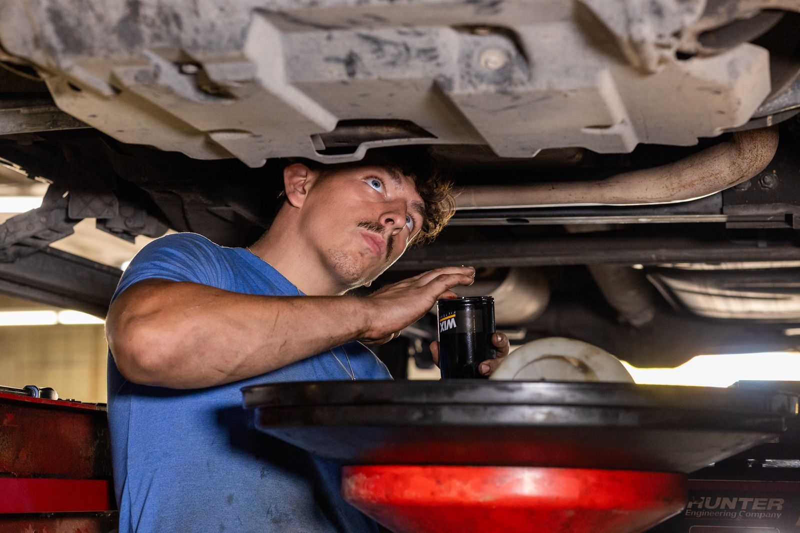 A service mechanic is working under a car in a garage.