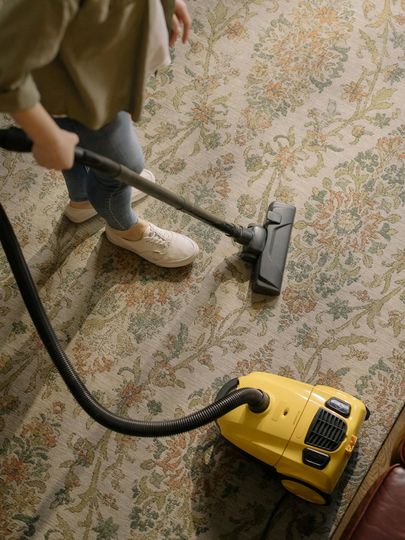 A person is vacuuming a rug with a yellow vacuum cleaner.