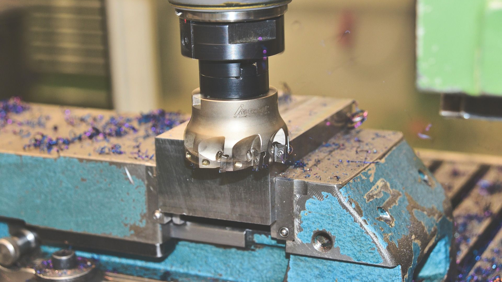 Milling machine cutting a metal block, blue and silver, covered in purple shavings.