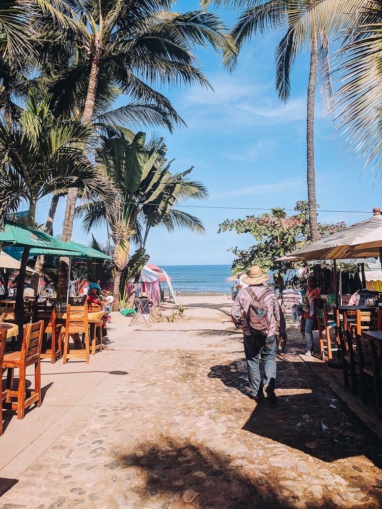 Un homme marche sur une plage bordée de tables et de chaises dans Sayulita, le village de la retraite