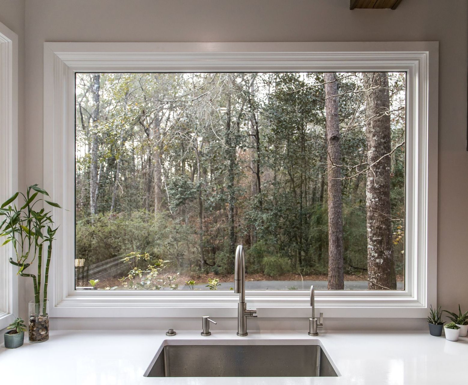 A kitchen sink with a large window overlooking the woods.