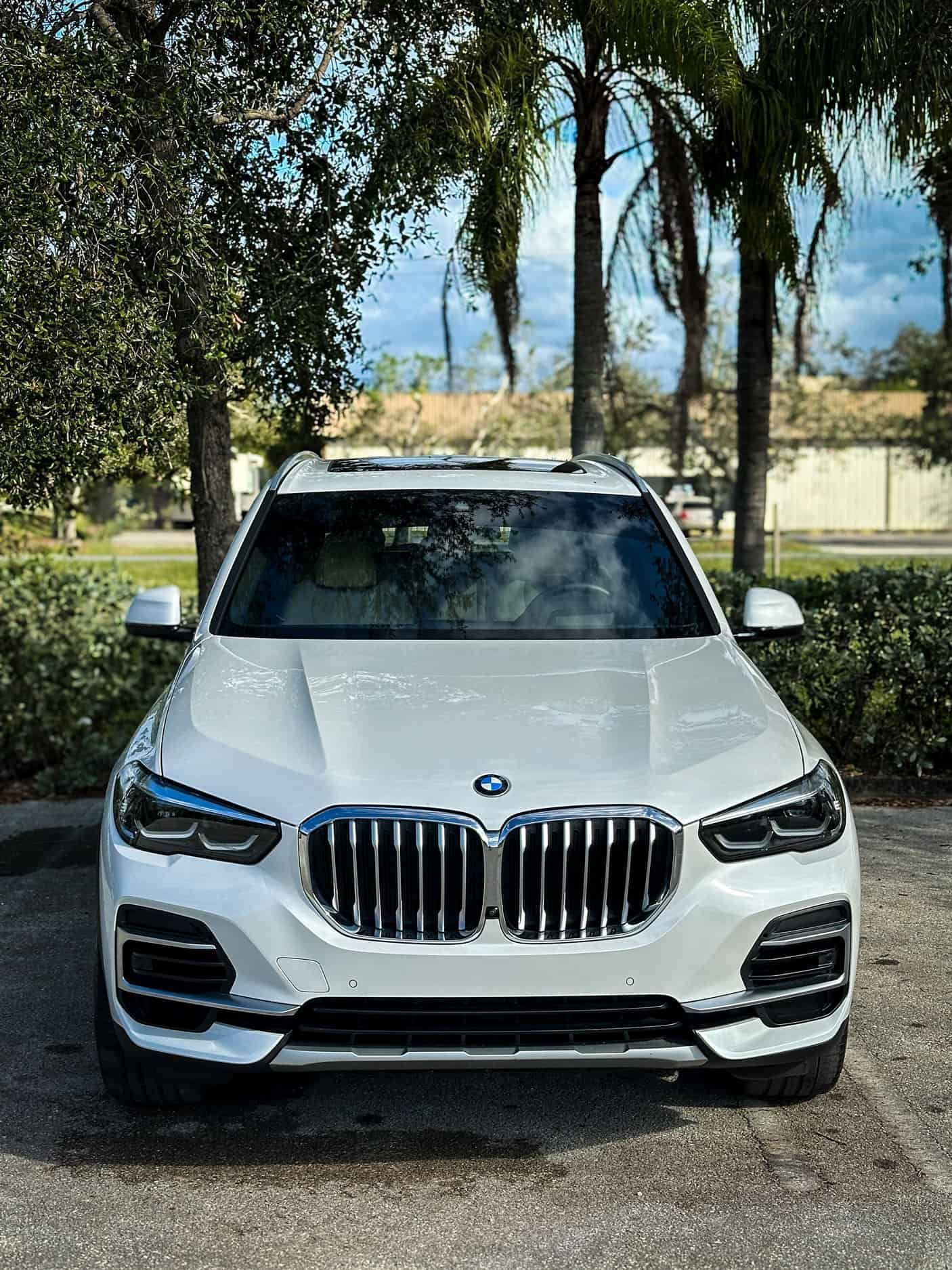 a Ceramic Coated White BMW X5 Facing the camera in a parking lot surrounded by trees in Melbourne, FL