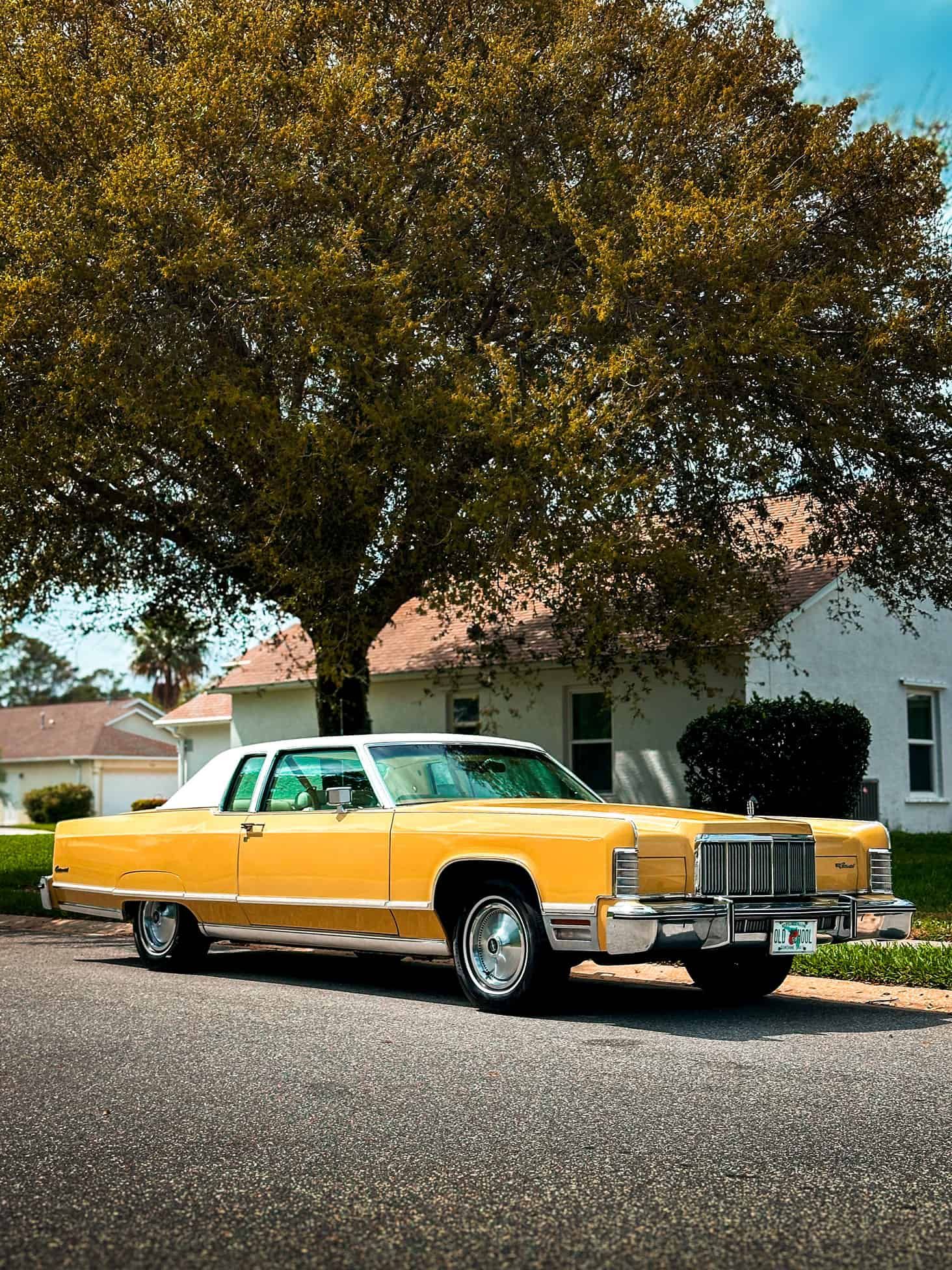 An all original 1973 Yellow Lincoln Town Car parked in the street with a large tree behind it in Palm Bay, Florida