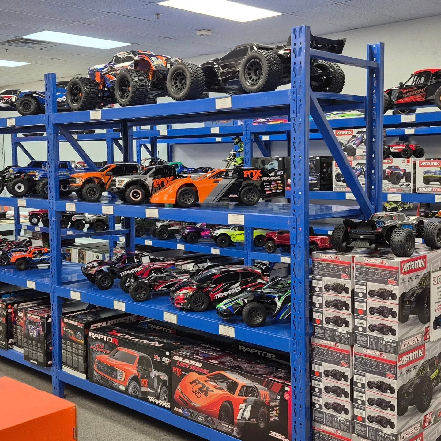 Shelves filled with various remote-controlled cars in a store, including trucks and race cars, in a blue-painted store.