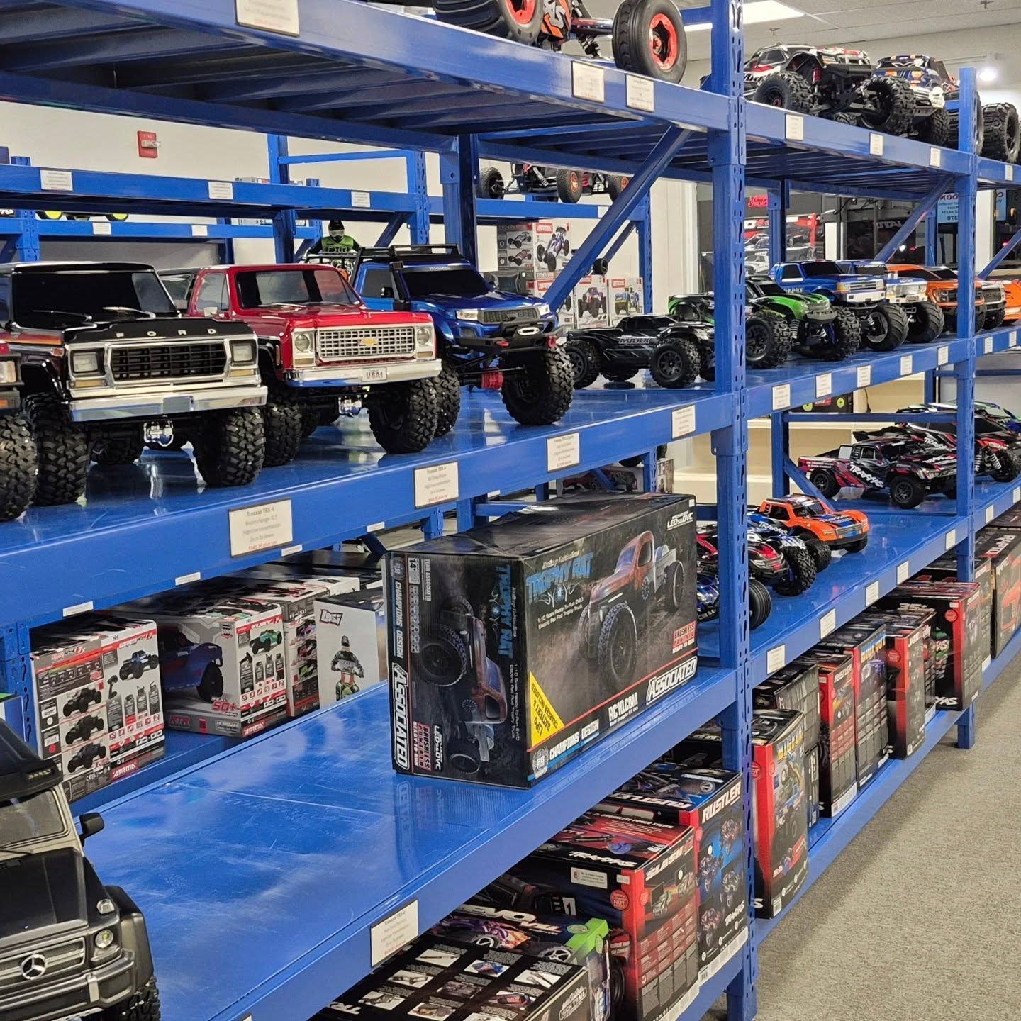 Shelves of blue metal stocked with remote control trucks and other toy vehicles in a store.