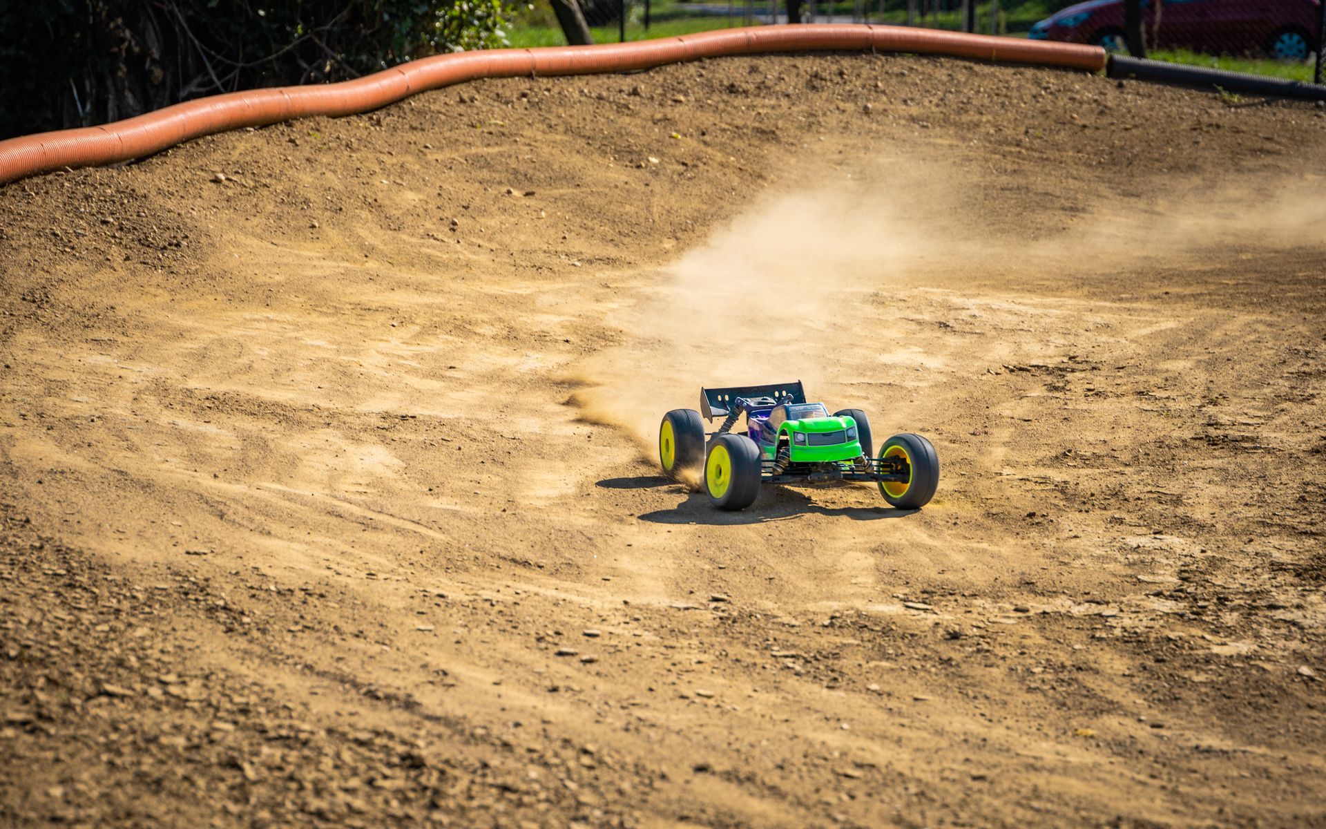 Green RC car racing on a dirt track, kicking up dust.