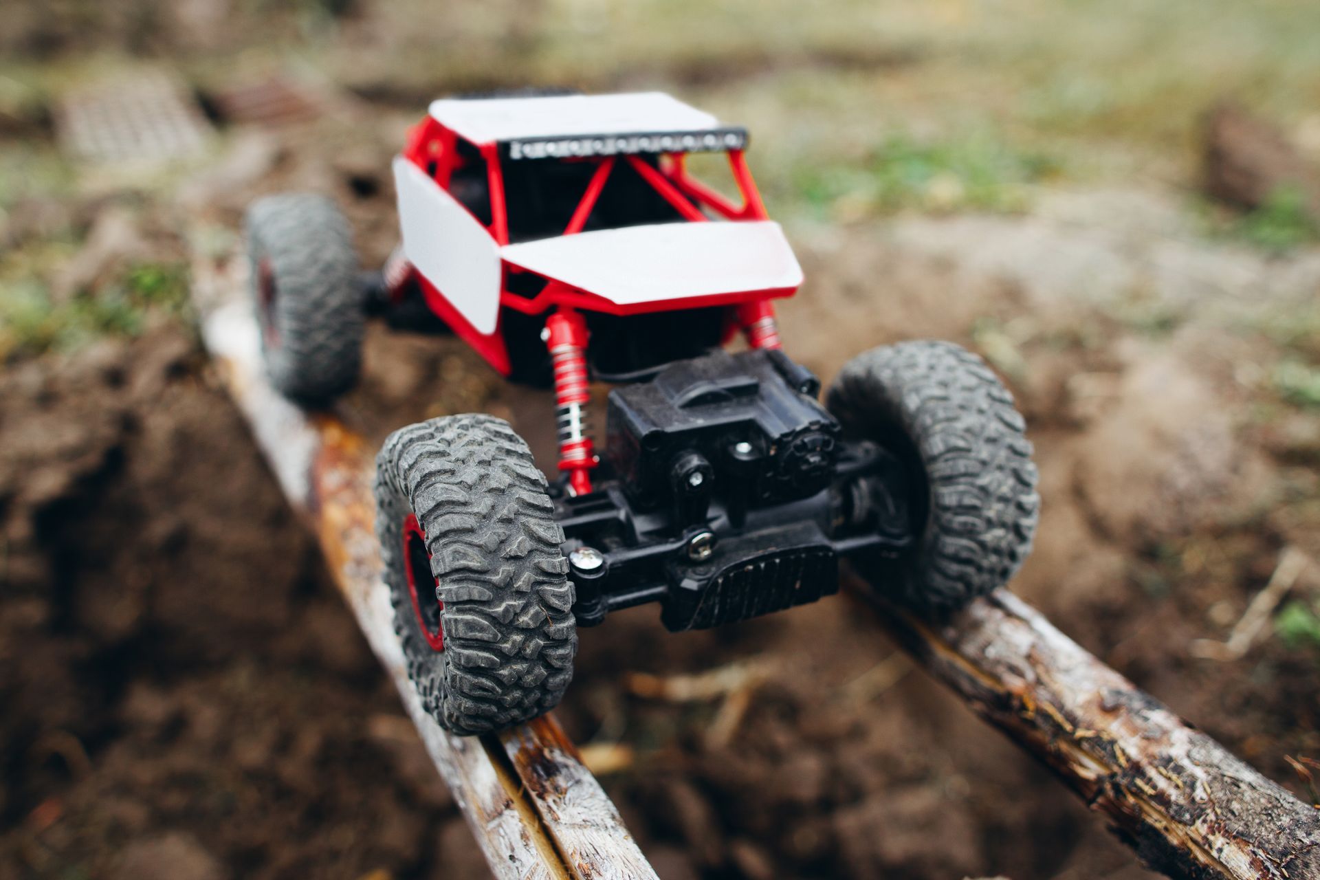 Red and white remote control off-road truck driving on wooden planks, muddy ground.