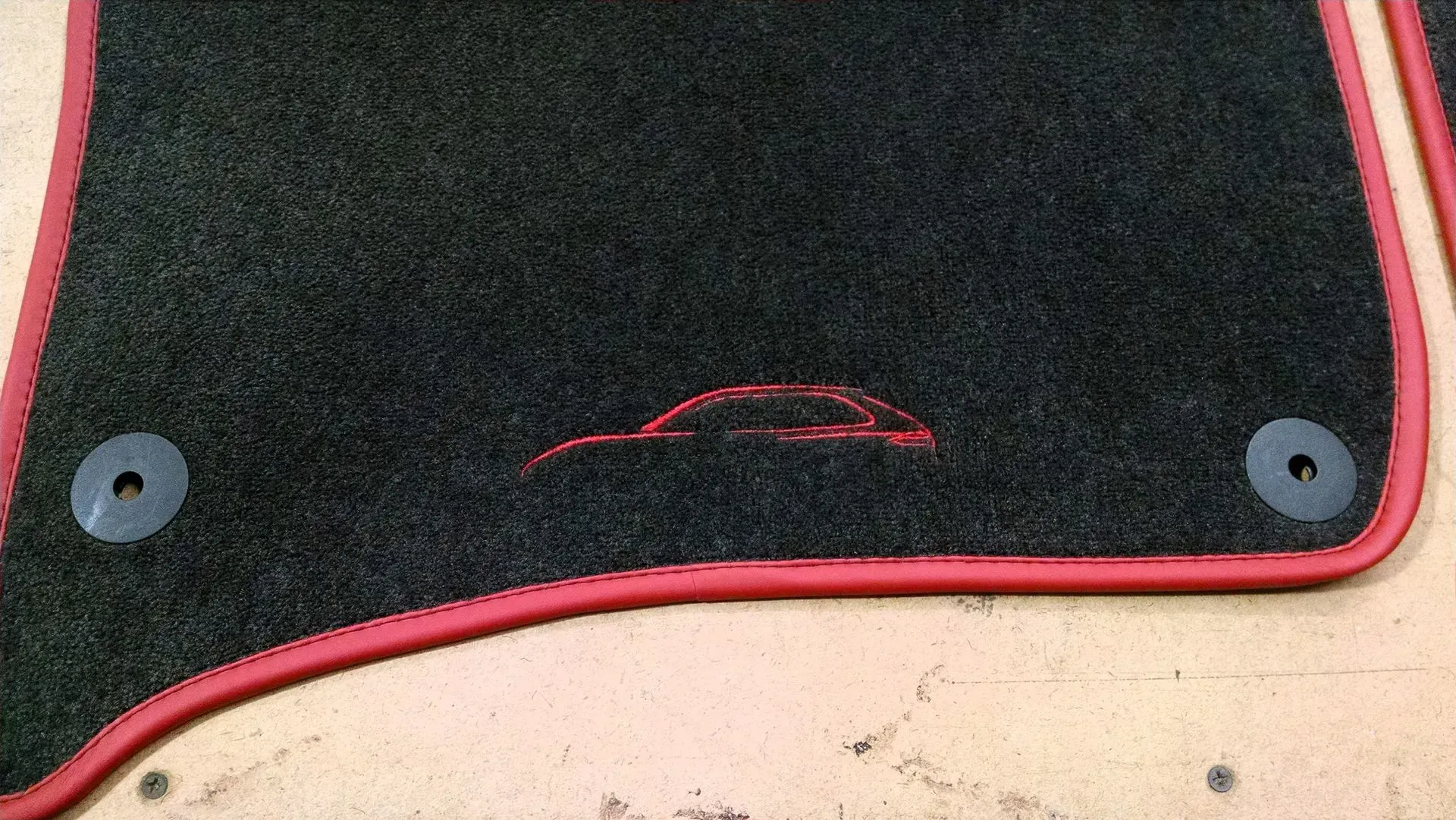 A close up of a black car mat with a red border.