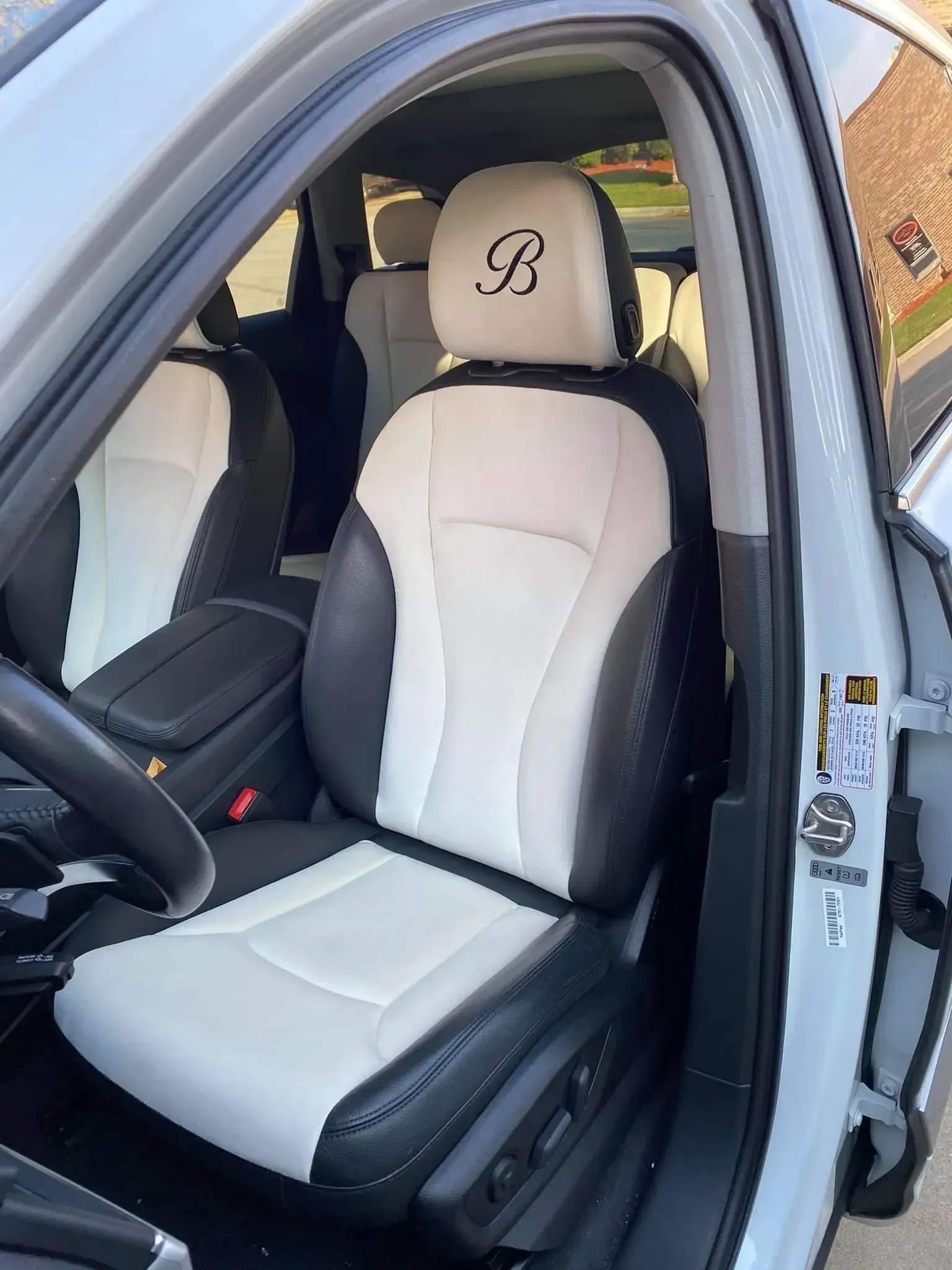 A white car with black seats and a monogram on the headrest.