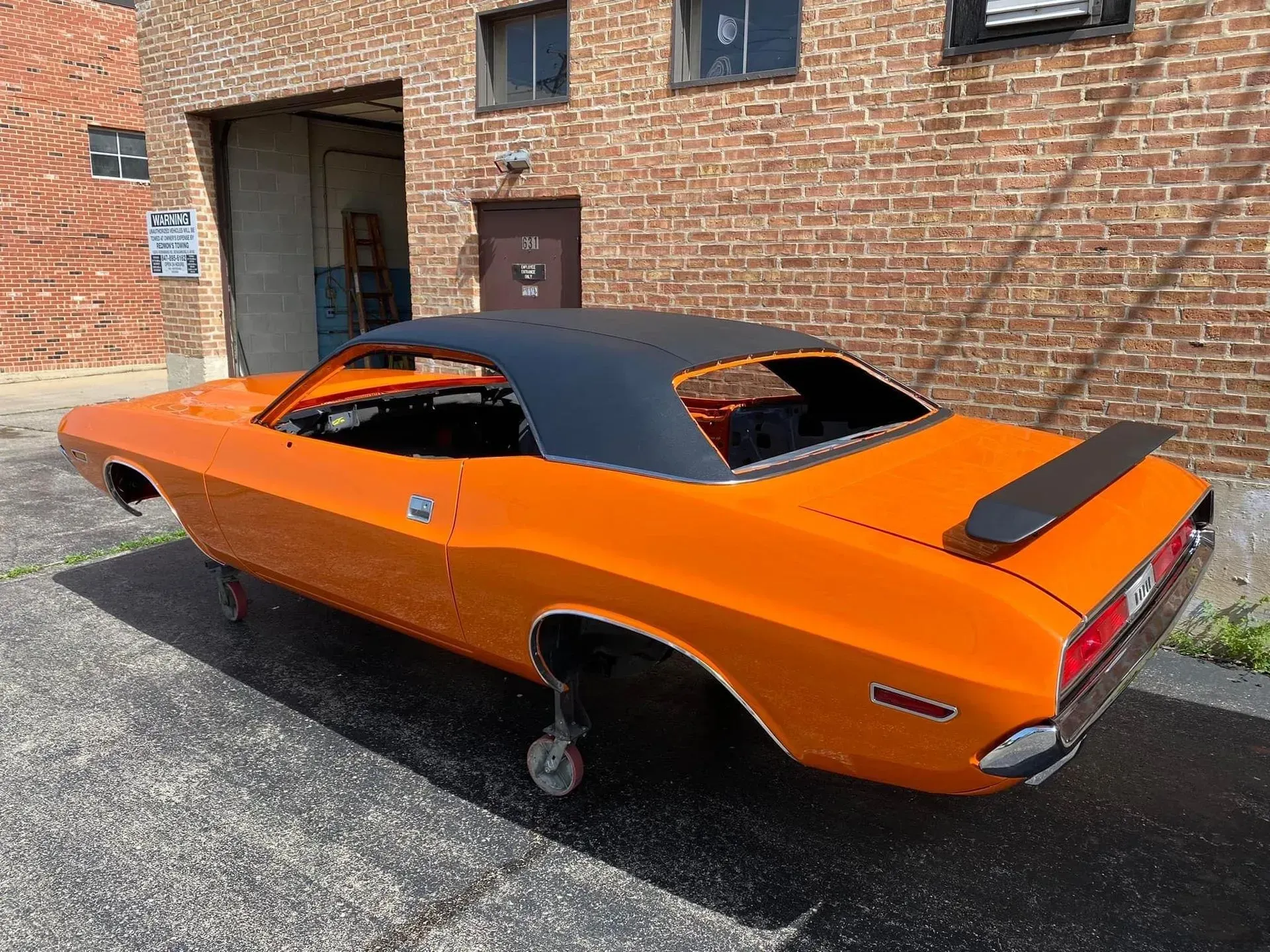 An orange dodge challenger is parked in front of a brick building.