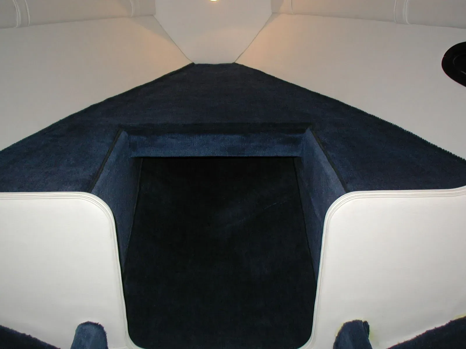 The inside of a boat with blue carpet and white seats
