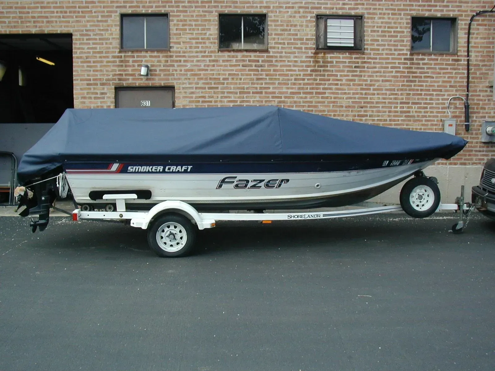 A fazer boat is on a trailer in front of a brick building