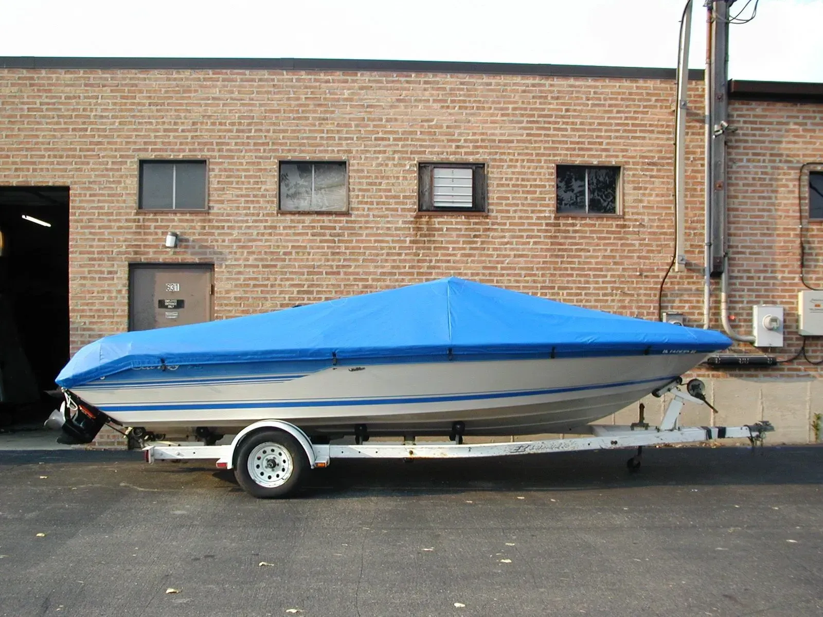 A boat with a blue cover on it is parked in front of a brick building