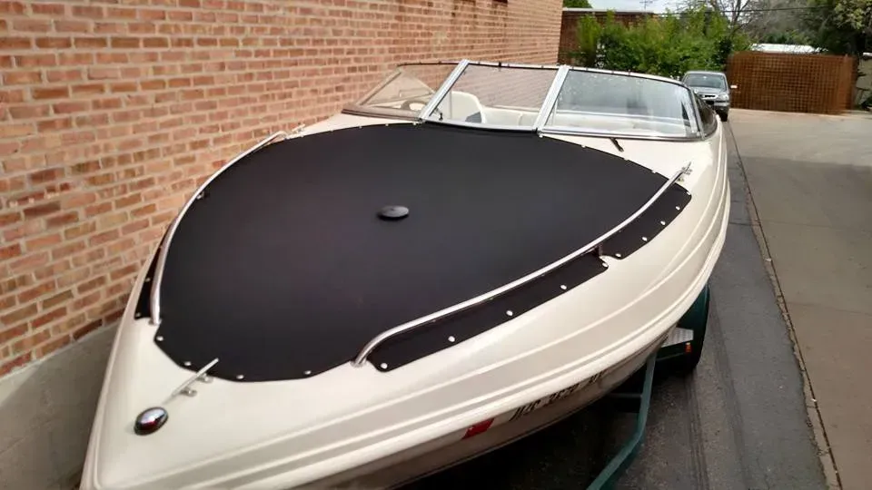 A white boat with a black cover is parked in front of a brick building.