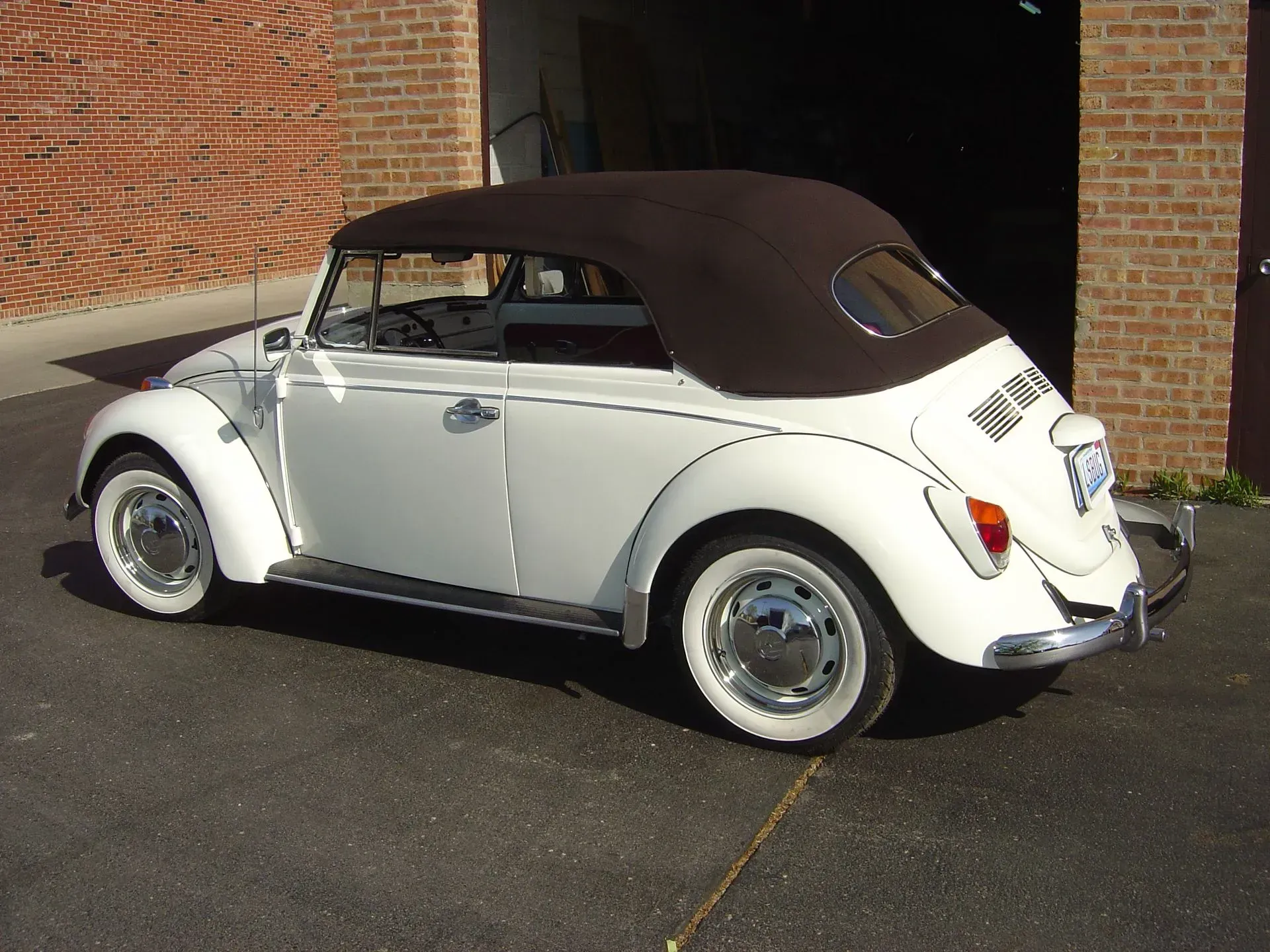 A white car with a brown top is parked in front of a brick building