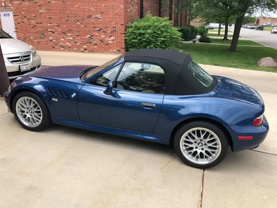 A blue bmw z3 convertible is parked in a driveway.