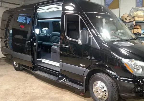 A black van is parked in a garage with its doors open.