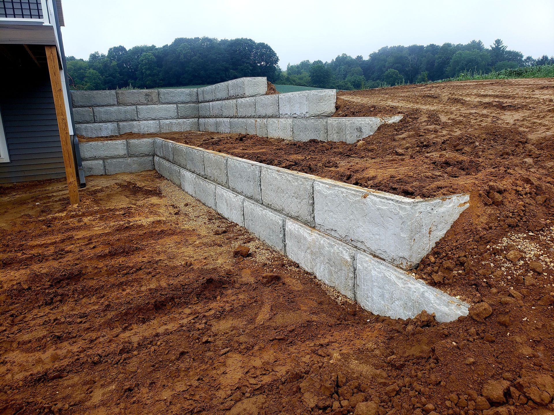 A concrete retaining wall is being built in a dirt field next to a house.