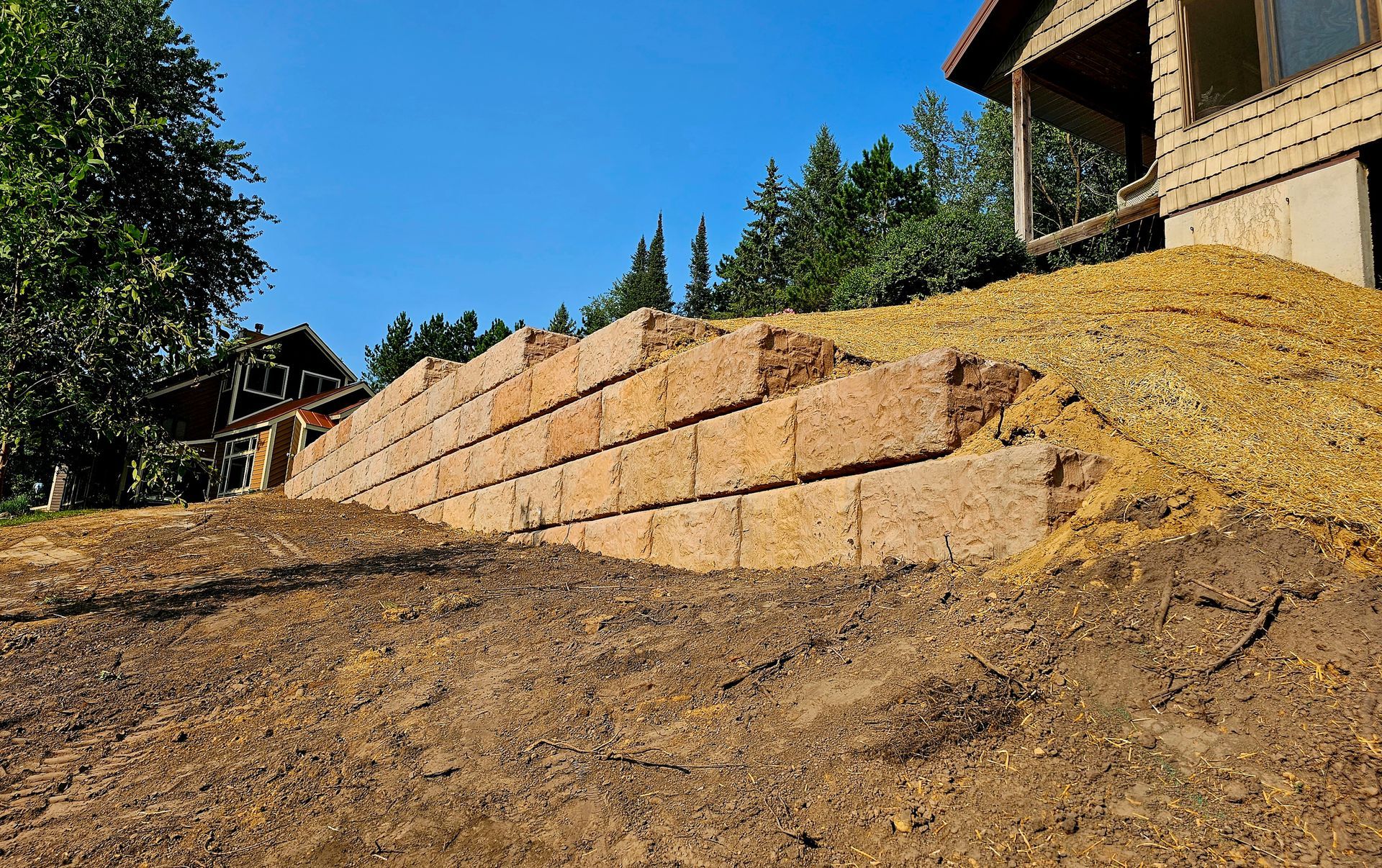 A large pile of dirt is sitting on top of a dirt hill next to a house.