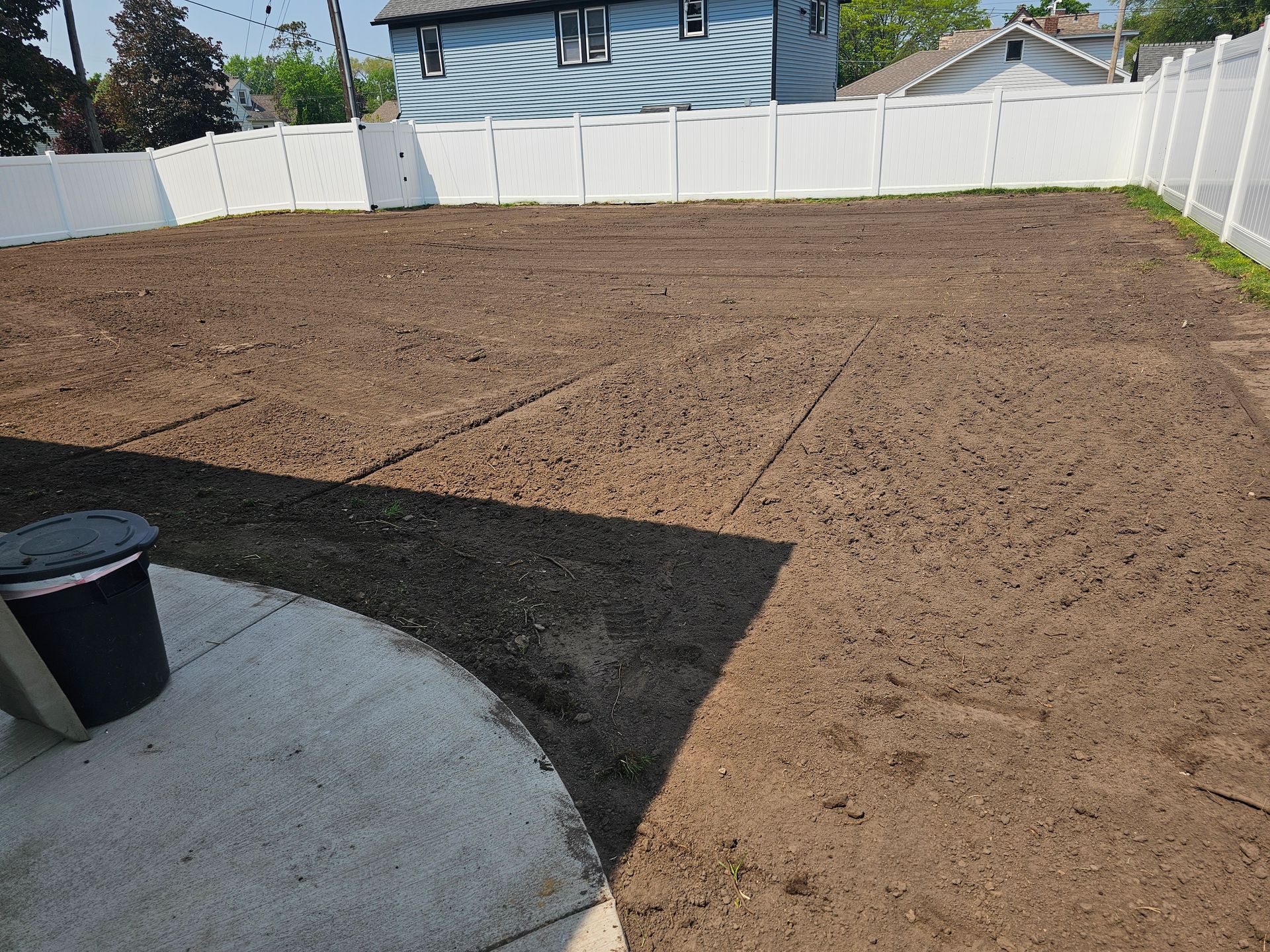 A backyard with a white fence and a lot of dirt.