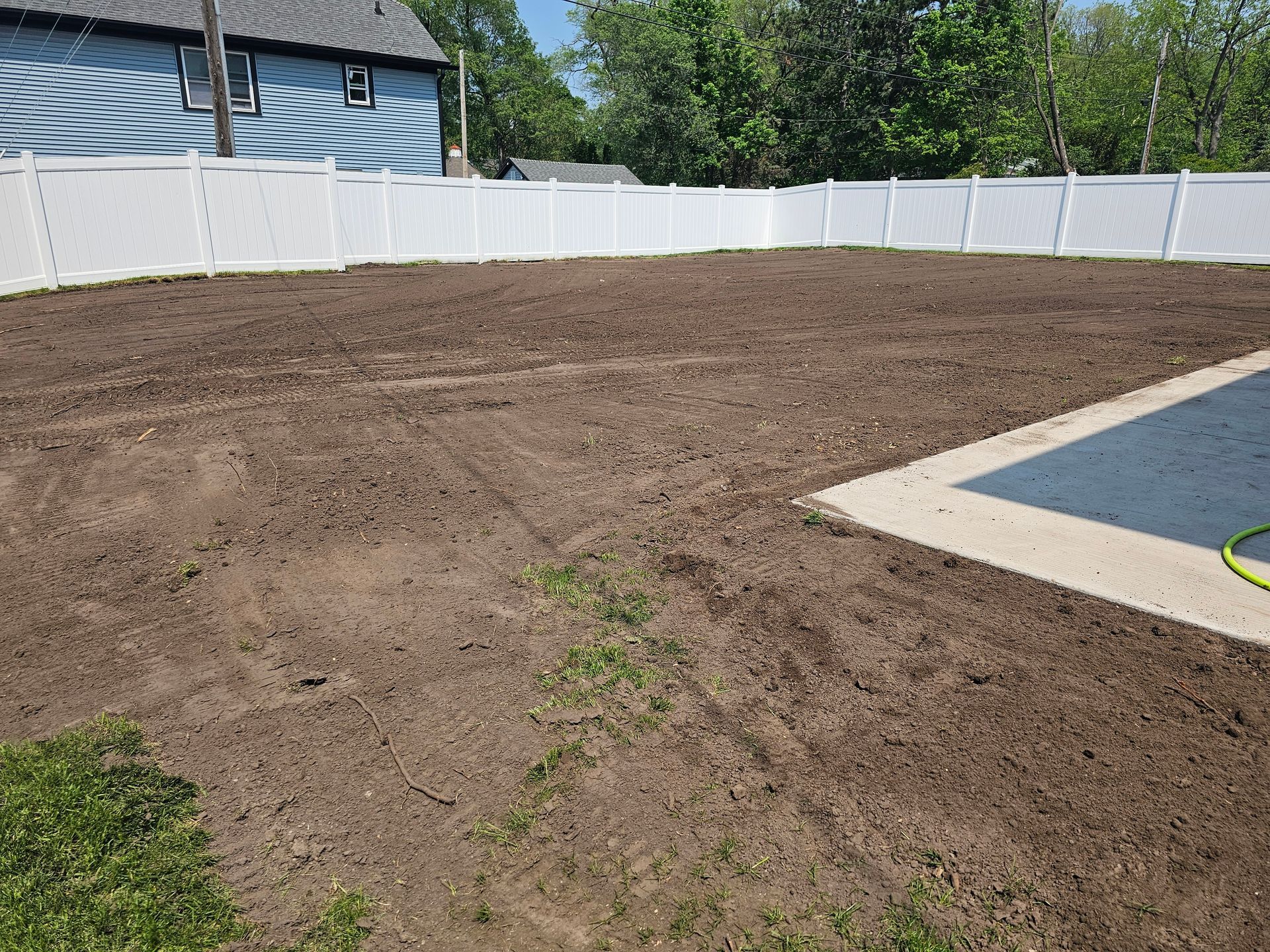 A backyard with a white fence and a pool in the background.
