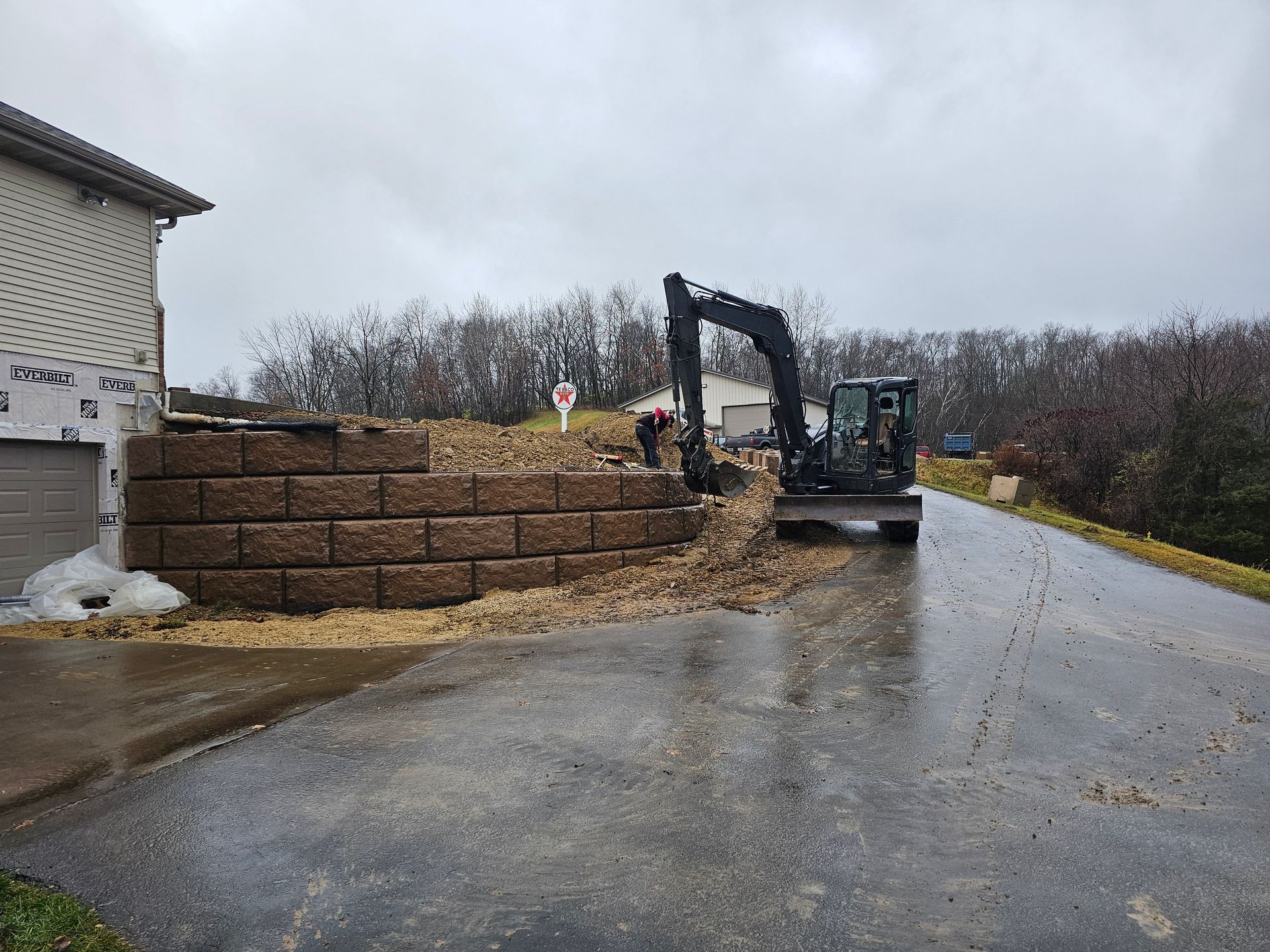 An excavator is working on a retaining wall in front of a house.