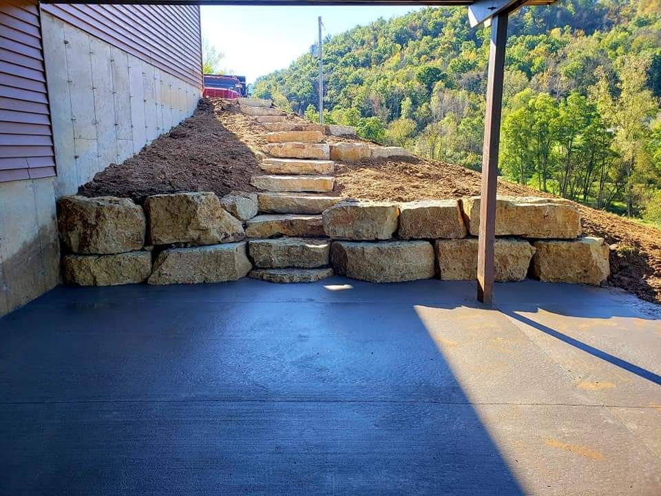 A concrete driveway with stairs leading up to a stone wall.