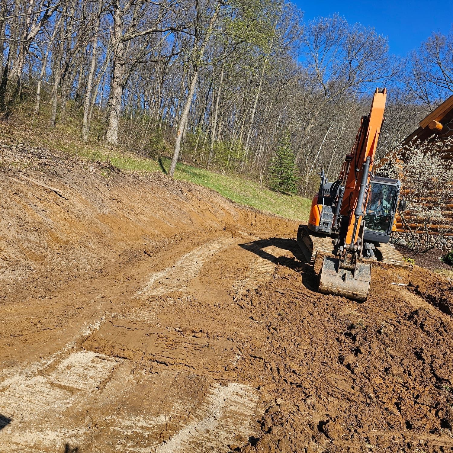 A large orange excavator is moving dirt on a dirt road.