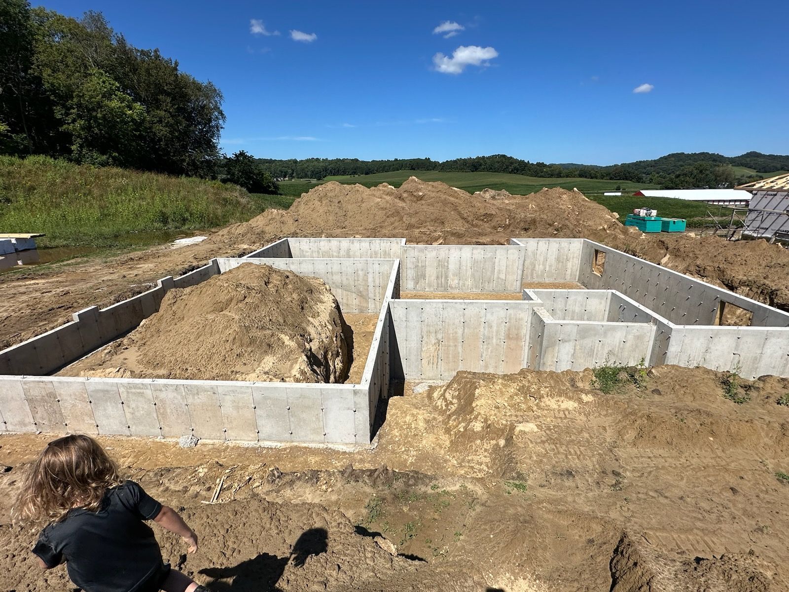 A little boy is playing in the dirt in front of a concrete foundation.