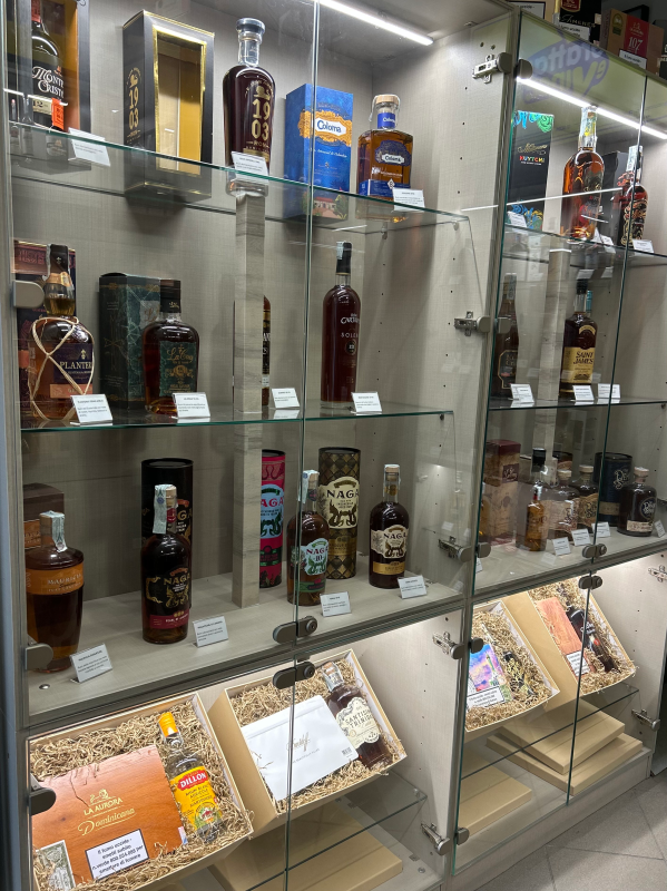 Bottiglie di liquore esposte in una vetrina illuminata, di varie forme e dimensioni, ripiani in legno.