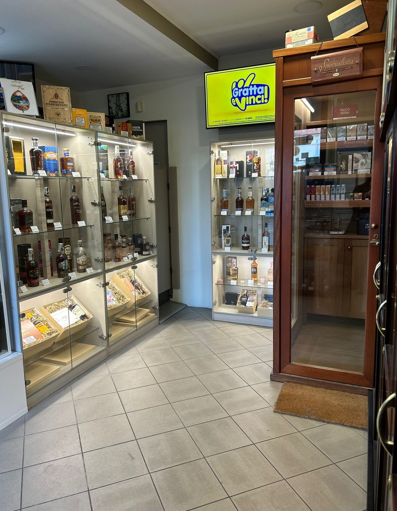 Interno di un negozio che espone bevande alcoliche in vetrine illuminate e in un mobiletto in legno.