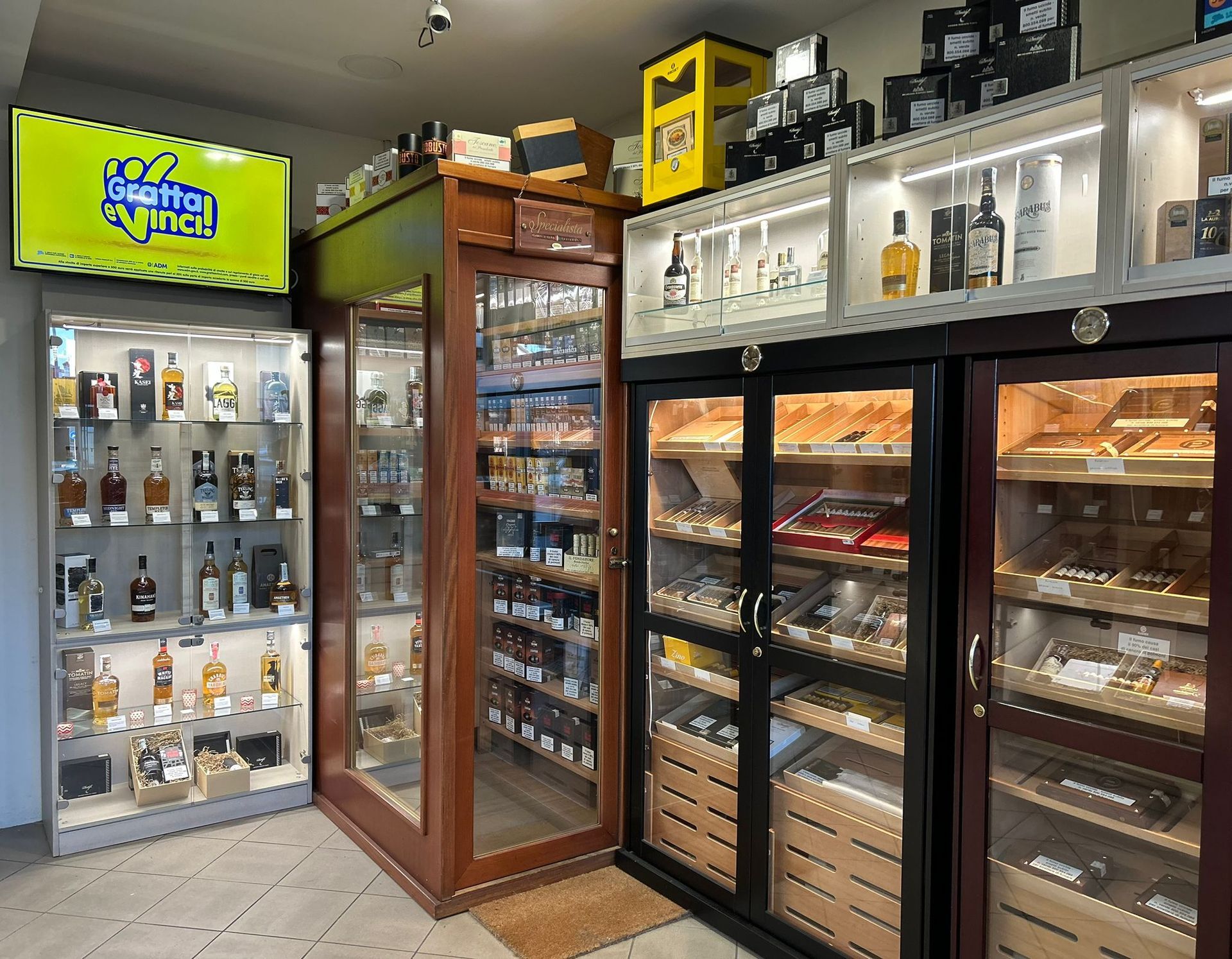 Interno di un negozio che espone sigari, liquori e altri prodotti in vetrine di vetro.
