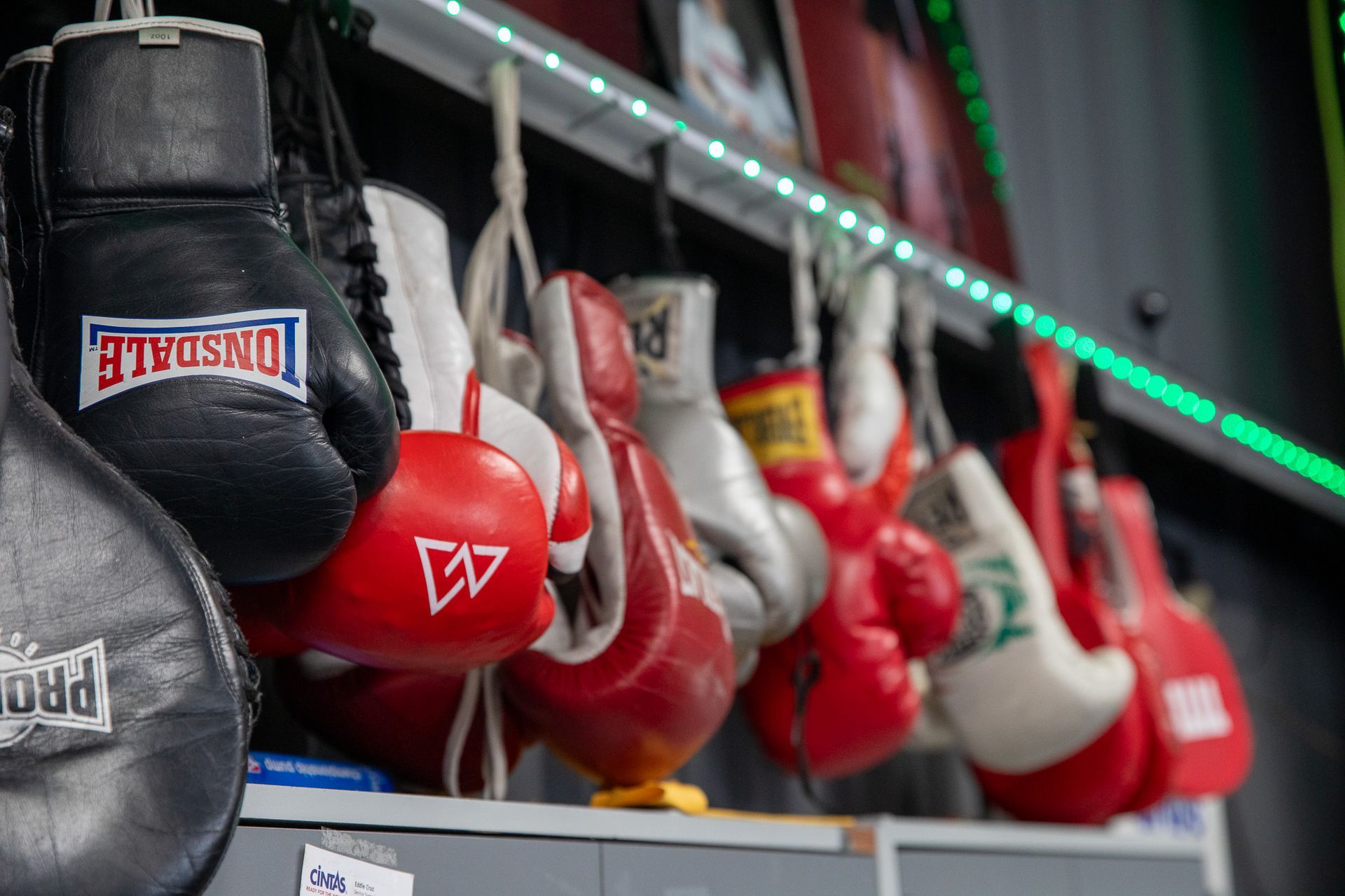 Boxing gloves hanging on a shelf in a gym. Black, red, and white gloves are visible.