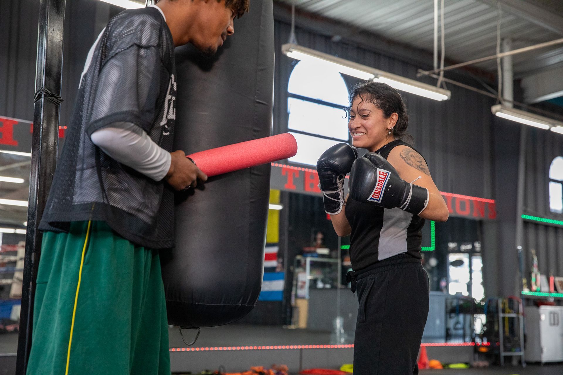 Woman boxing with trainer at gym; he holds a pad.