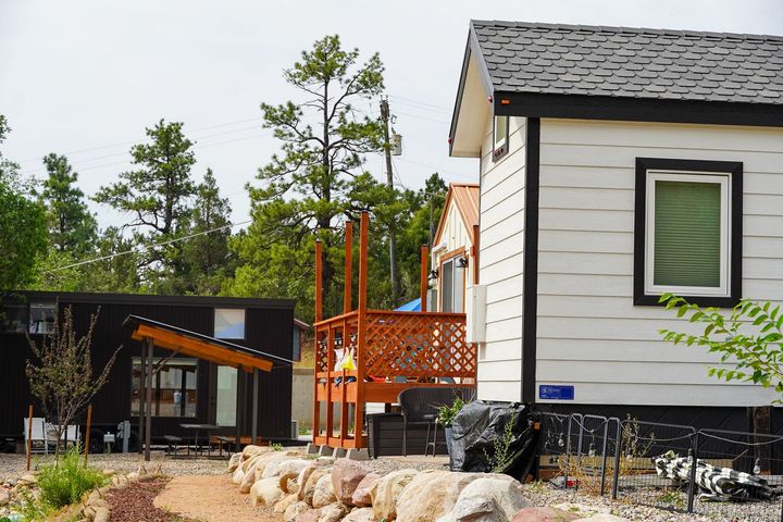 Two modern cabins with decks in a wooded area. The primary cabin is white with black trim.