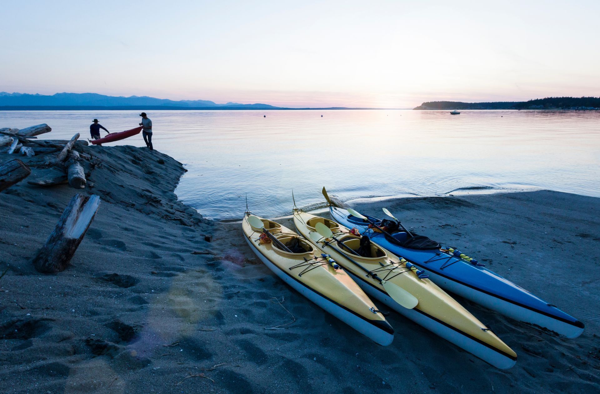 Three kayaks are sitting on the beach near the water.