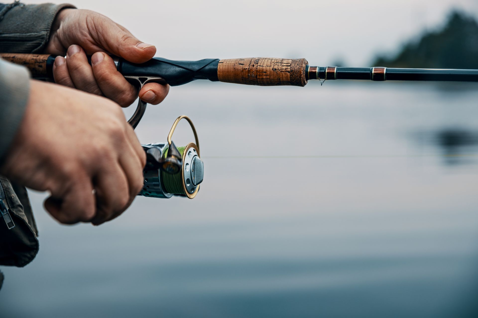 A person is holding a fishing rod in their hands in front of a body of water.