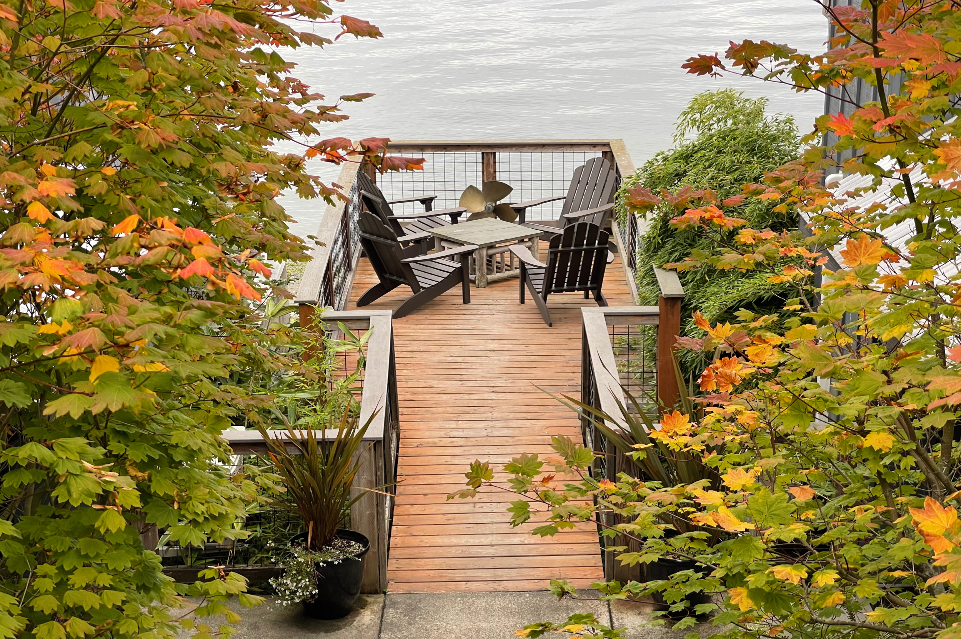 A wooden deck with chairs and a table overlooking a body of water surrounded by trees.