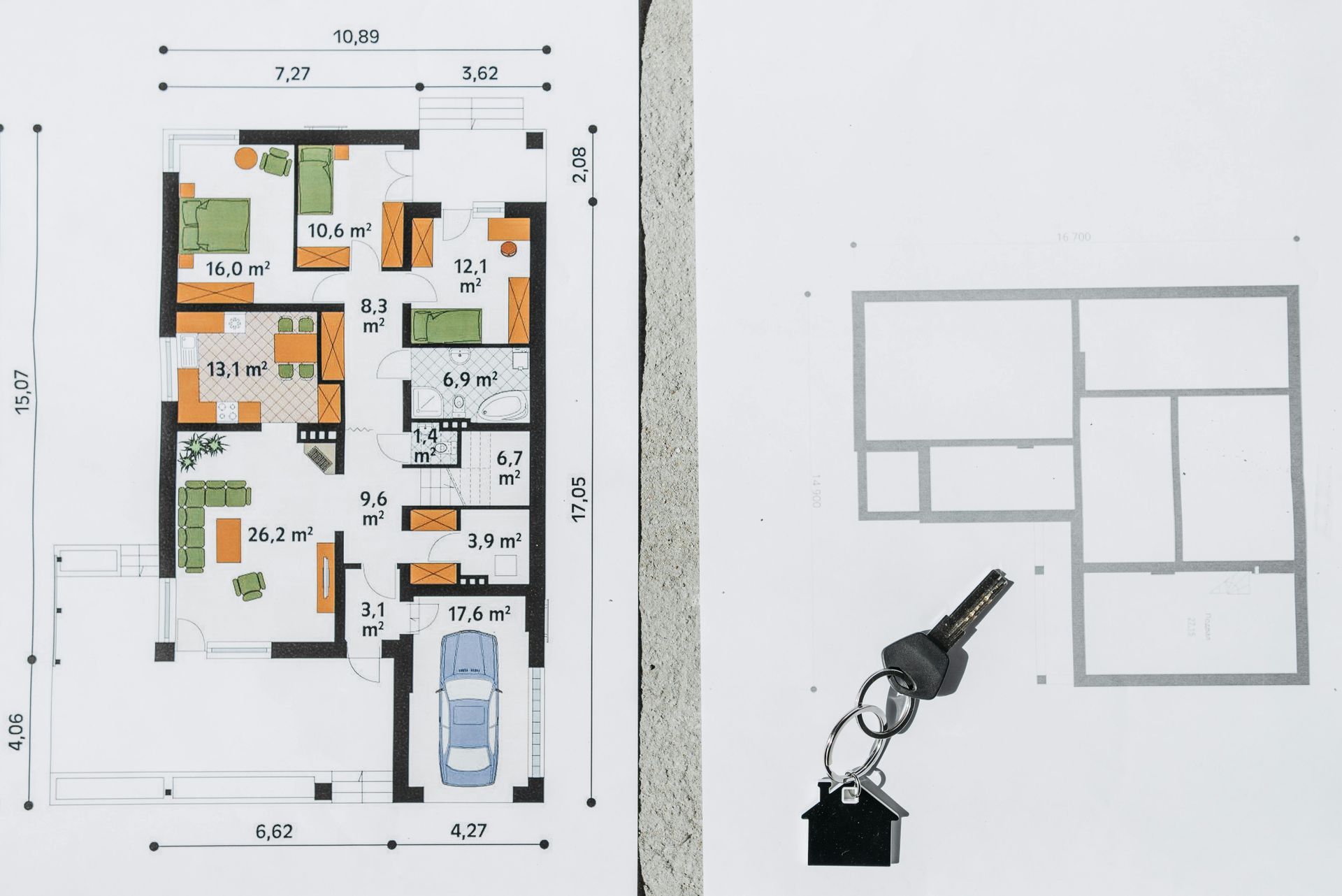 Floor plan and key on a white surface, blueprint with room dimensions and colors, and a key with a house-shaped charm.