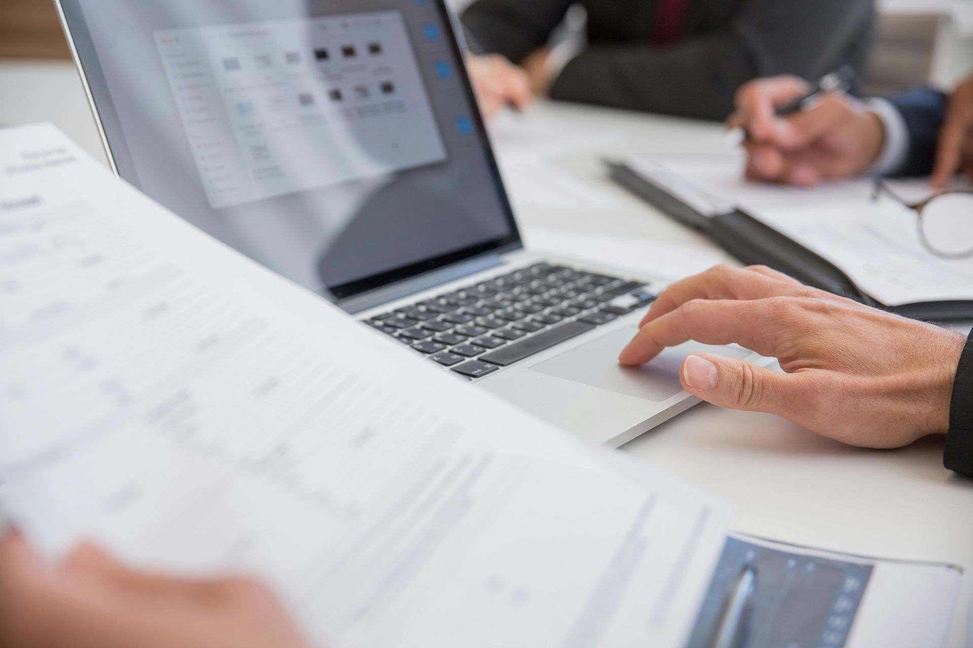 Person's hand on laptop touchpad, reviewing documents in a business meeting.