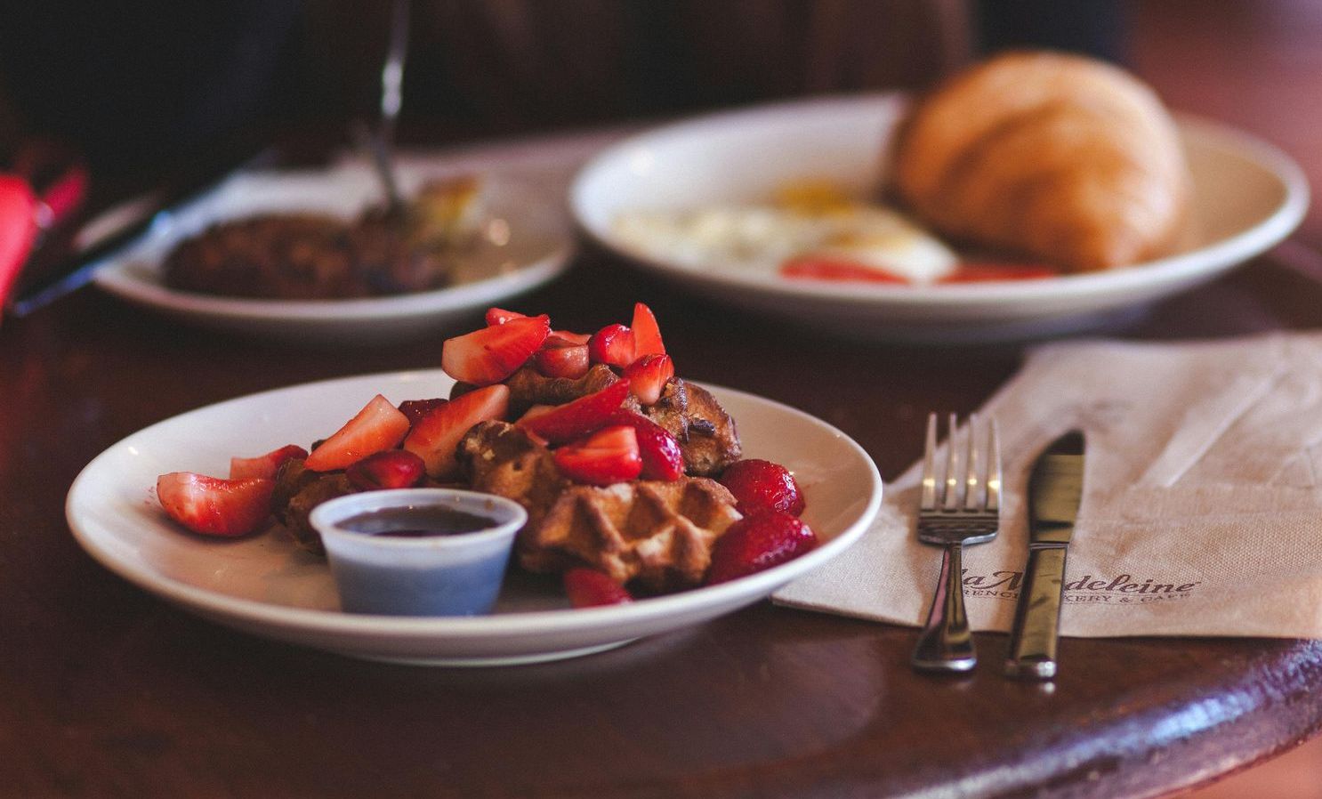 A plate of waffles with strawberries and chocolate sauce on a table.