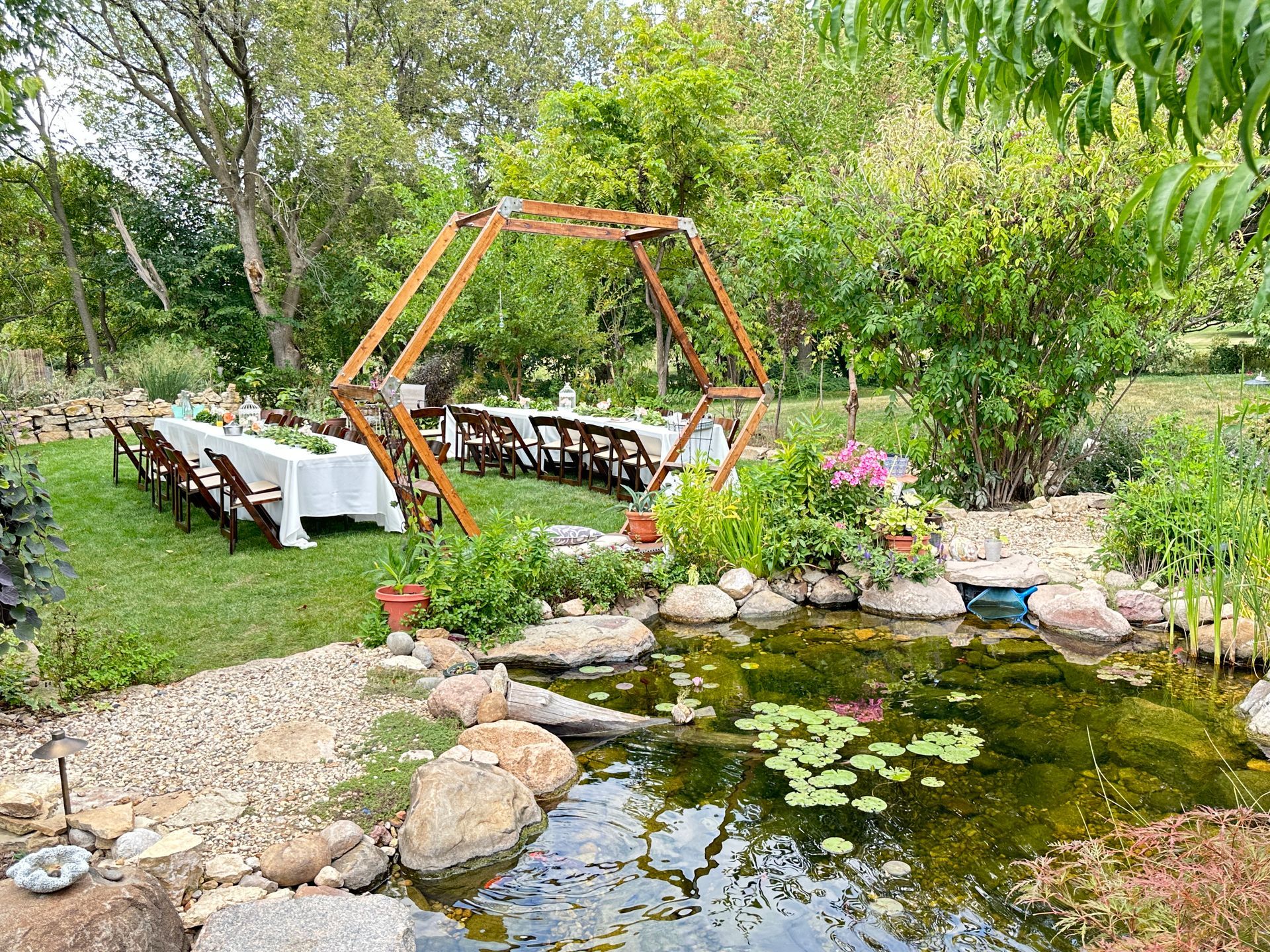 A table and chairs are set up in a garden next to a pond.
