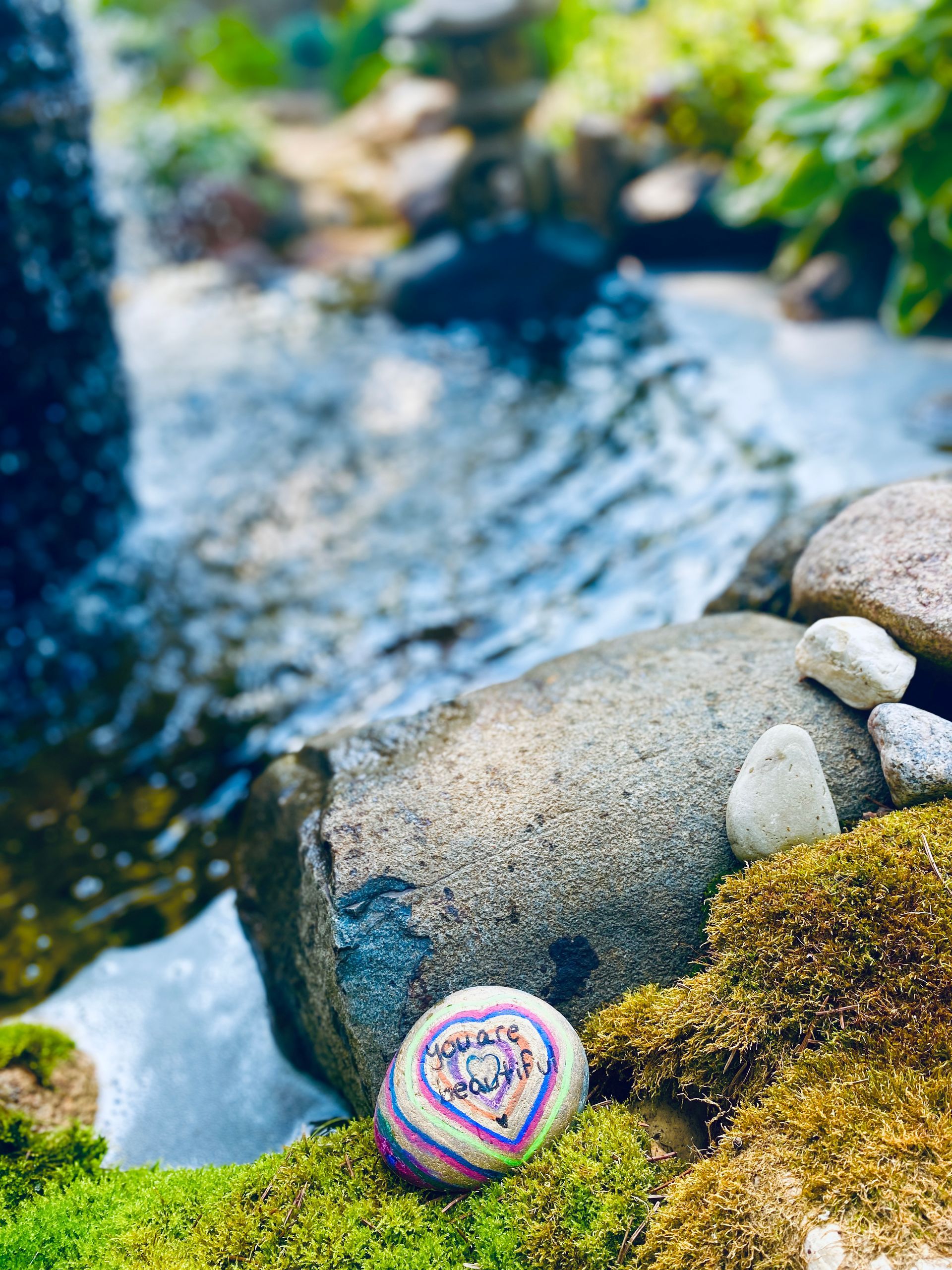 A rock is sitting on top of a pile of moss next to a stream.