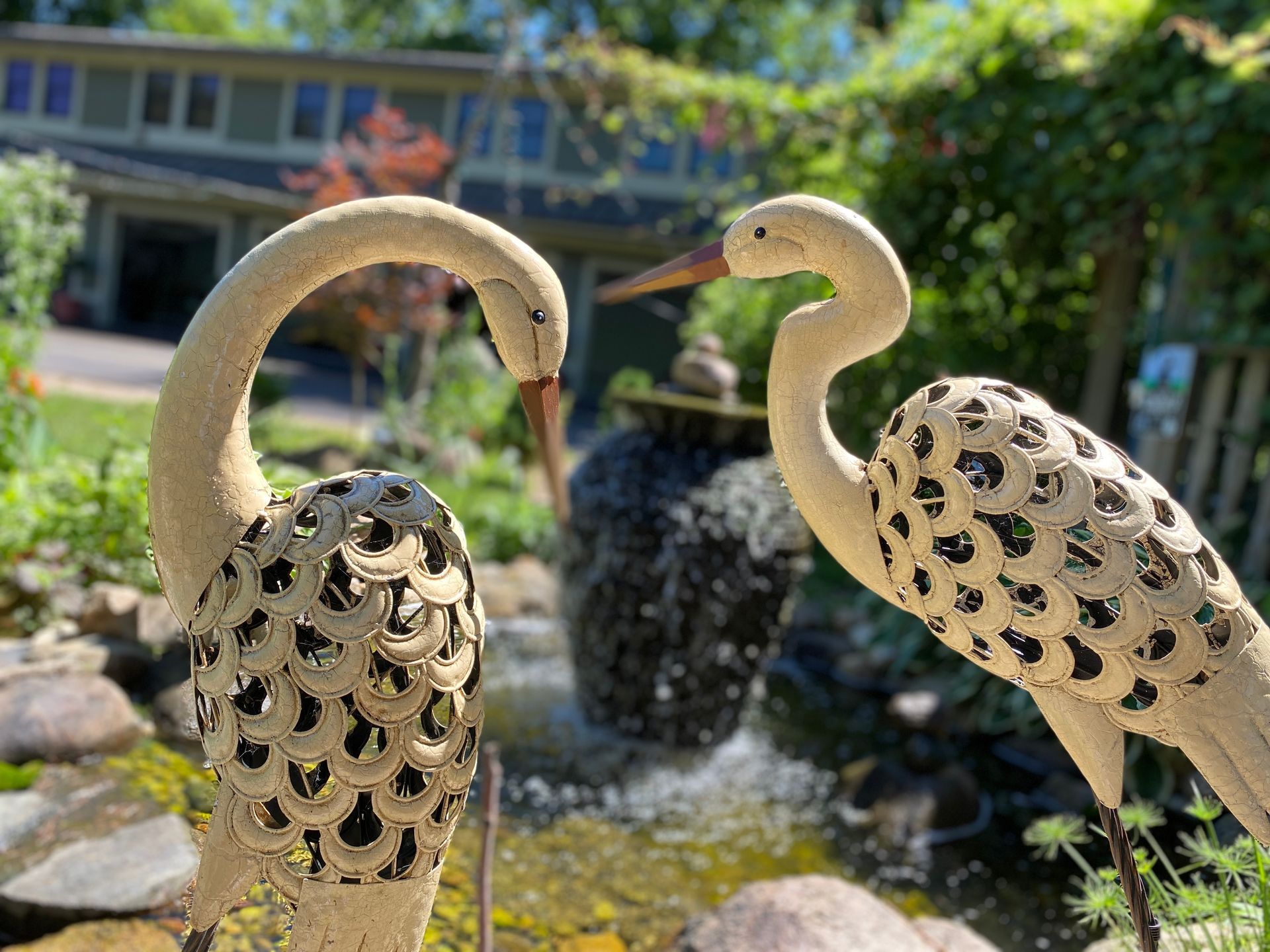 Two statues of birds are standing next to each other in front of a pond.