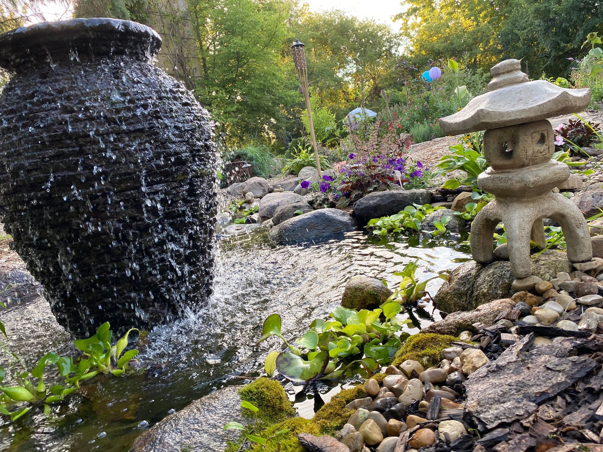 A fountain in a garden with a vase and a lantern in the foreground.