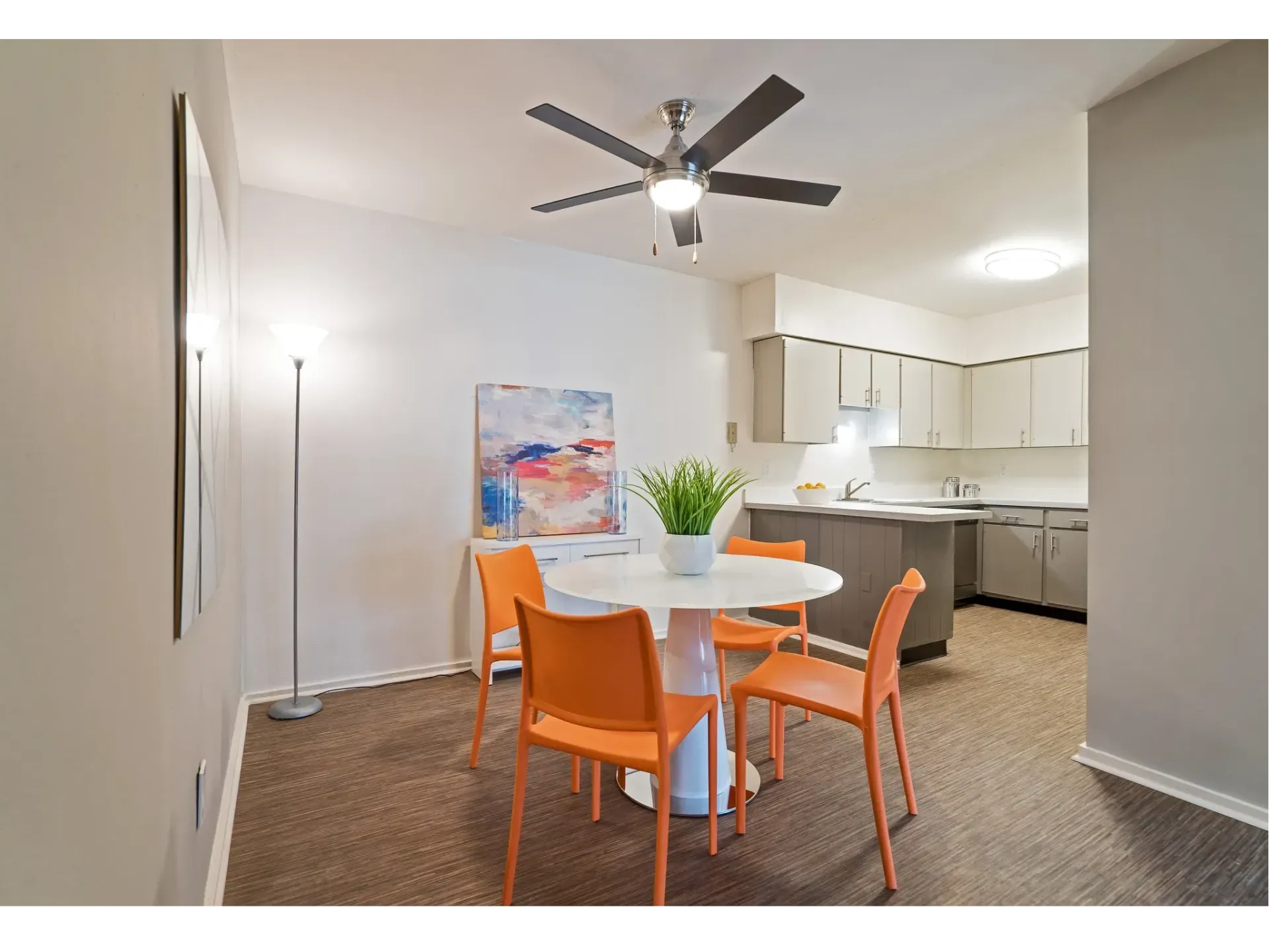 Dining area with a round table, orange chairs, and kitchen in the background